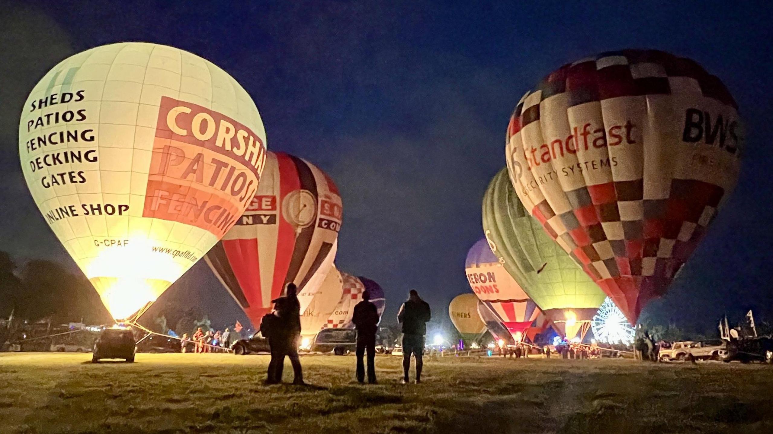 People stand silhouetted among hot air balloons as they fire their burners at the Bristol Balloon Fiesta