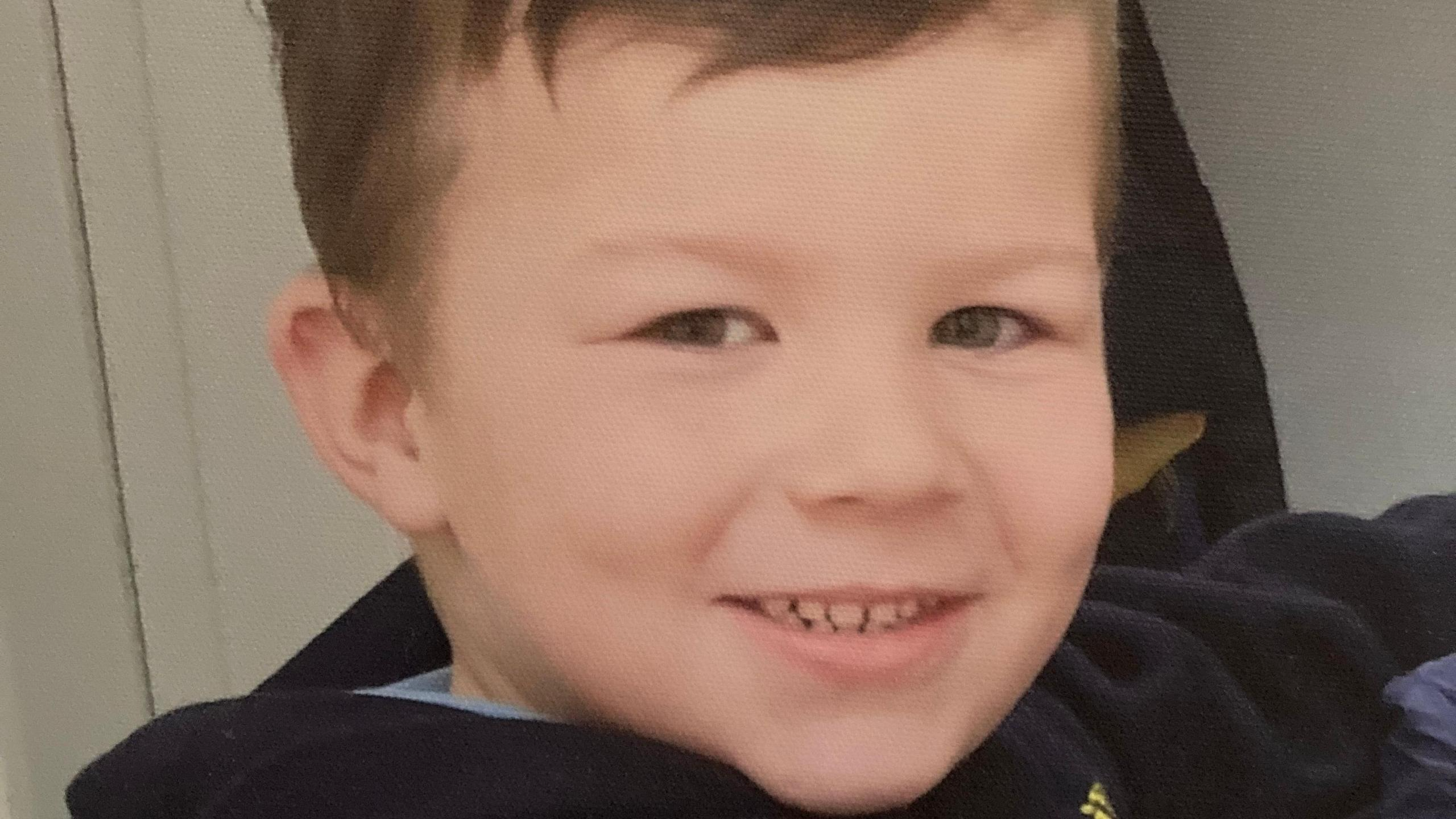 Caio, the victim of a dog attack, smiling at the camera. The young boy has short brown hair and brown eyes and wearing a dark jumper.