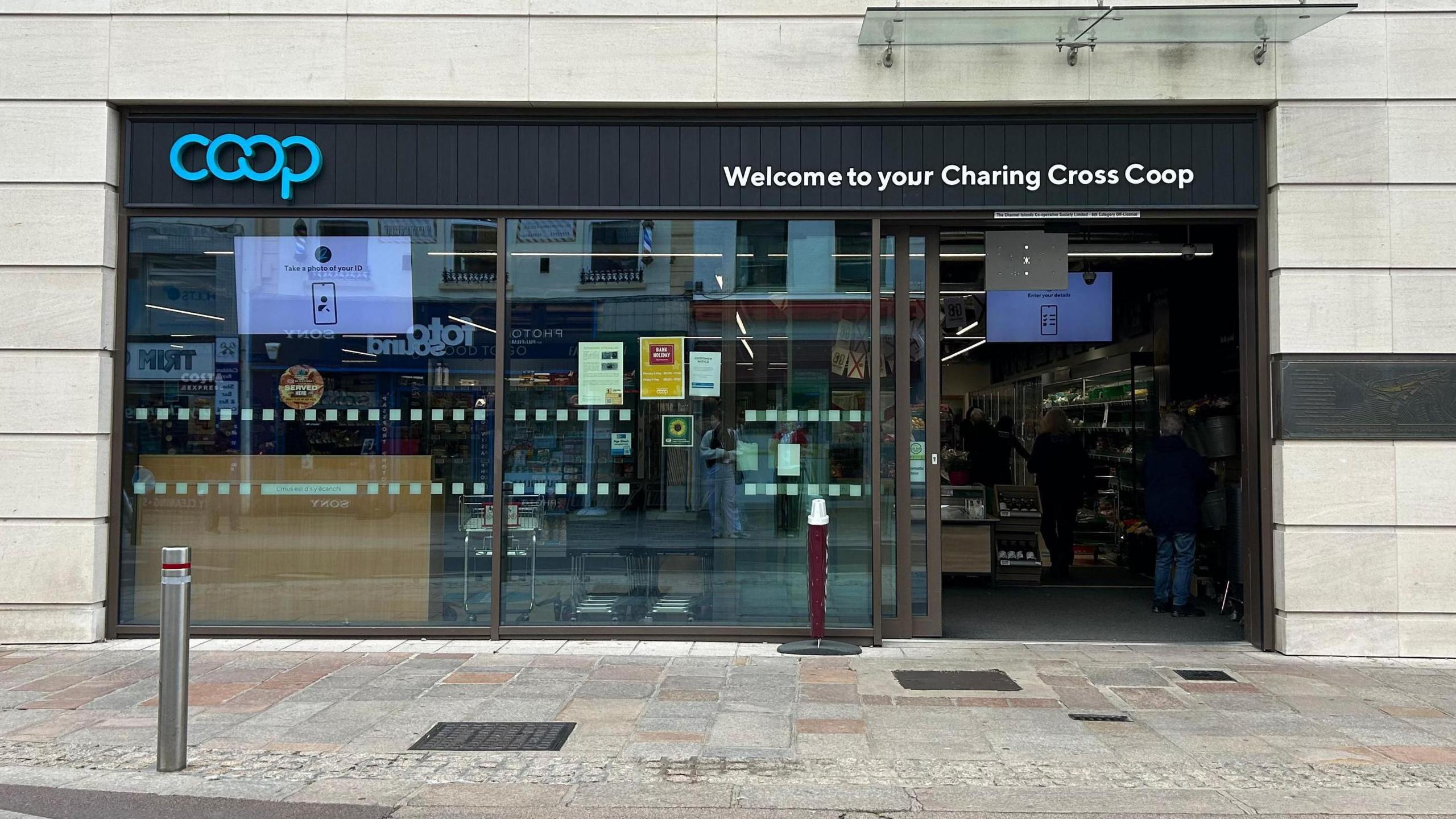 The Coop which says 'welcome to your Charing Cross Coop'. There is an automatic door that is open and is made of glass.