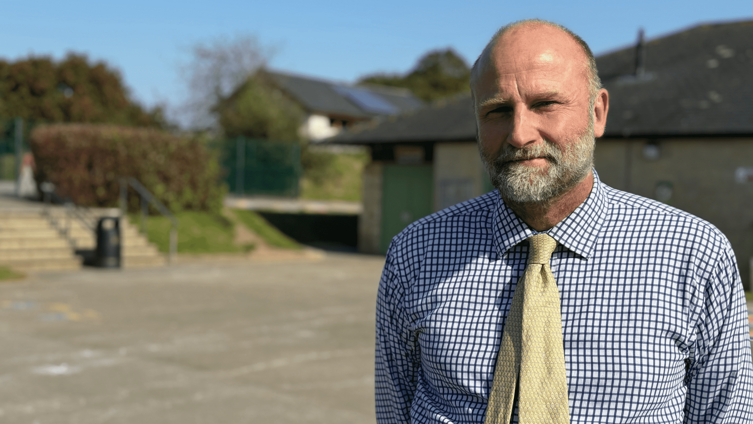 Nick Moss standing in a school playground with a checked shirt and yellow tie