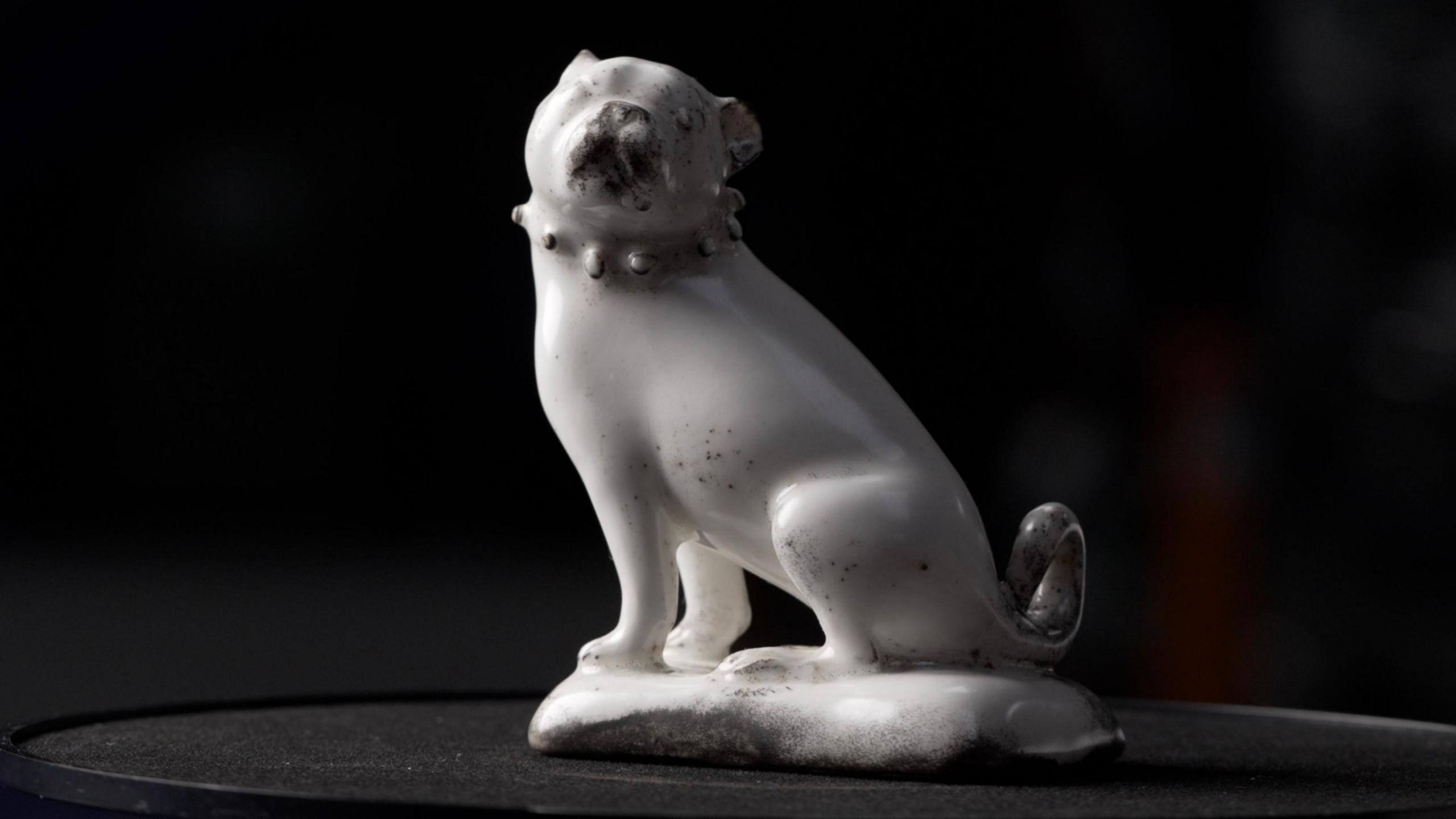 A complete figurine of a seated pug dog in plain white glazed porcelain with details picked out in black found at St James' Euston