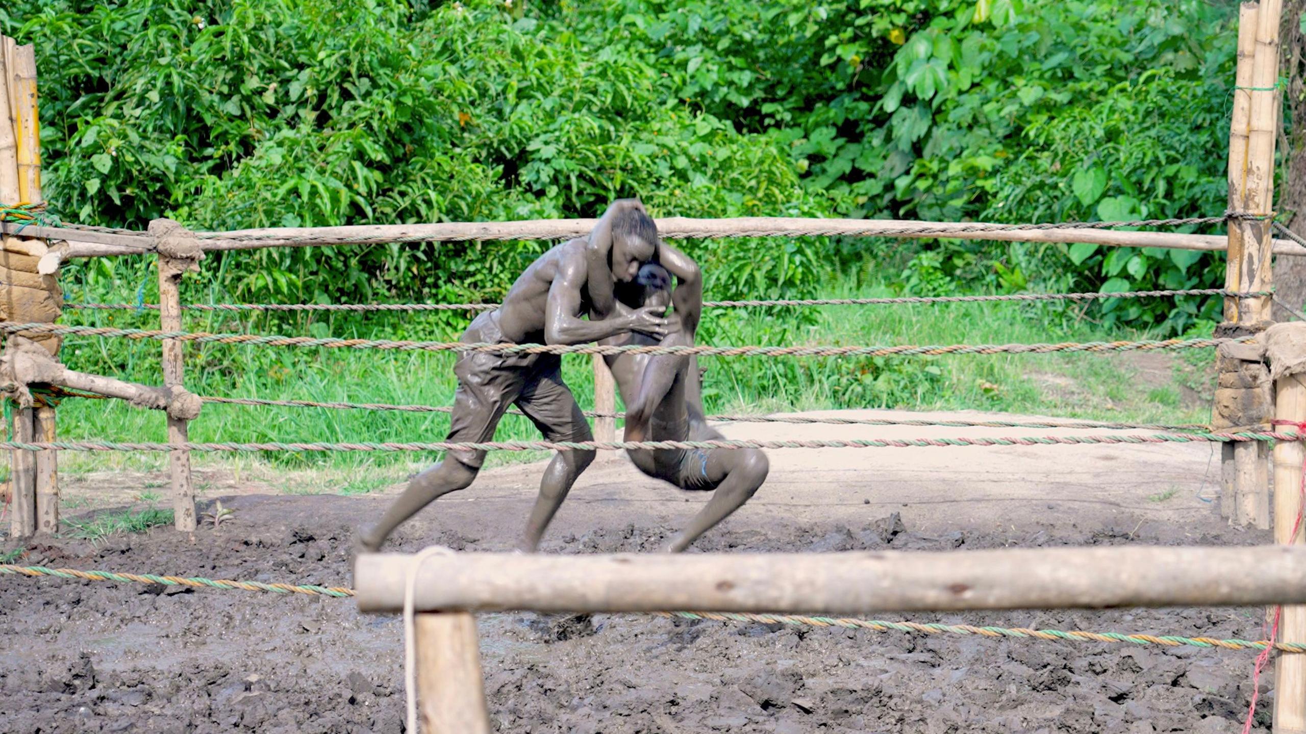 Two men wrestle in a mud ring in Uganda