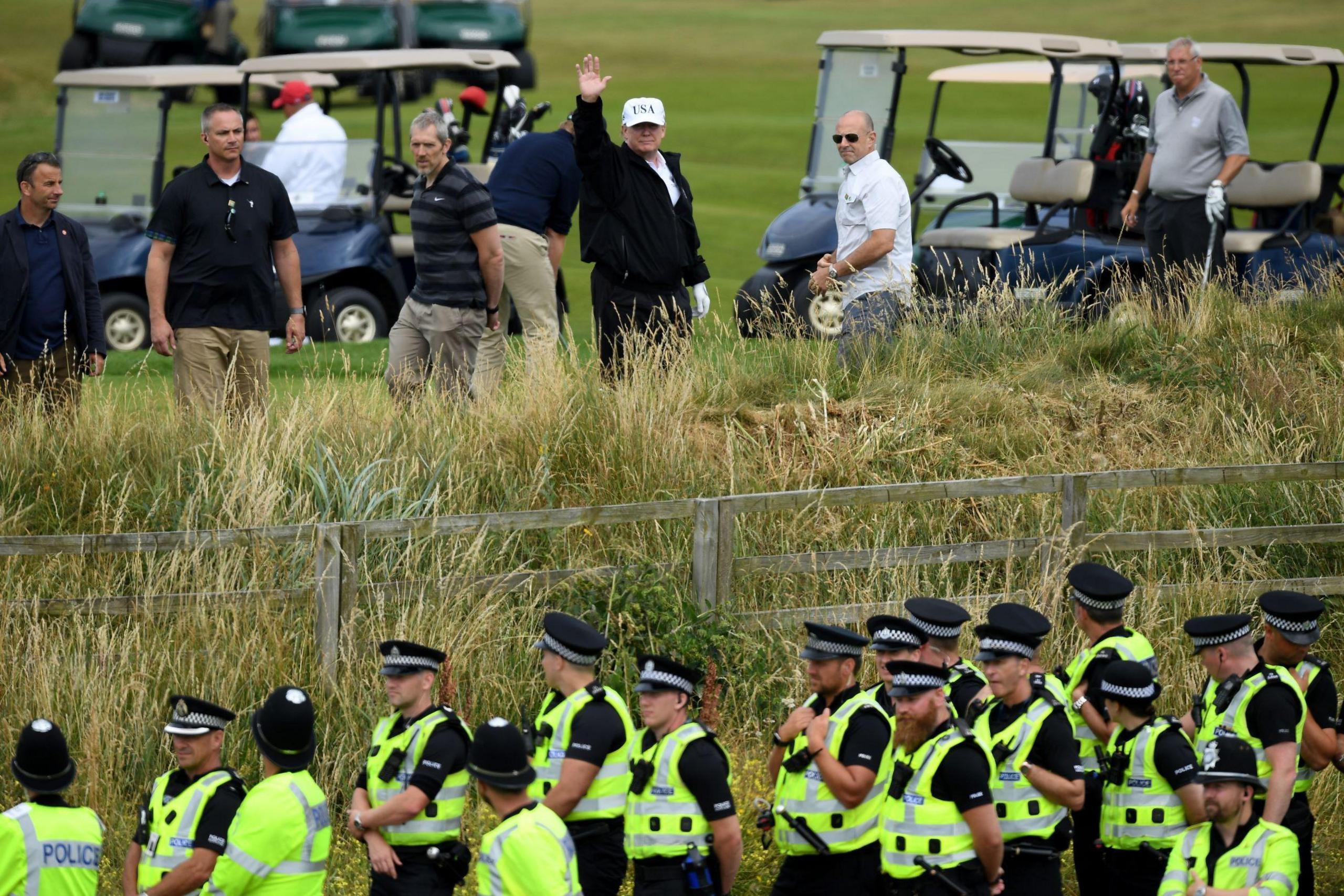 Police secure the area as U.S. President Donald Trump, wearing a white hat with Trump and USA displayed on it, waves while playing golf at Trump Turnberry Luxury Collection Resort during the President's first official visit to the United Kingdom.
