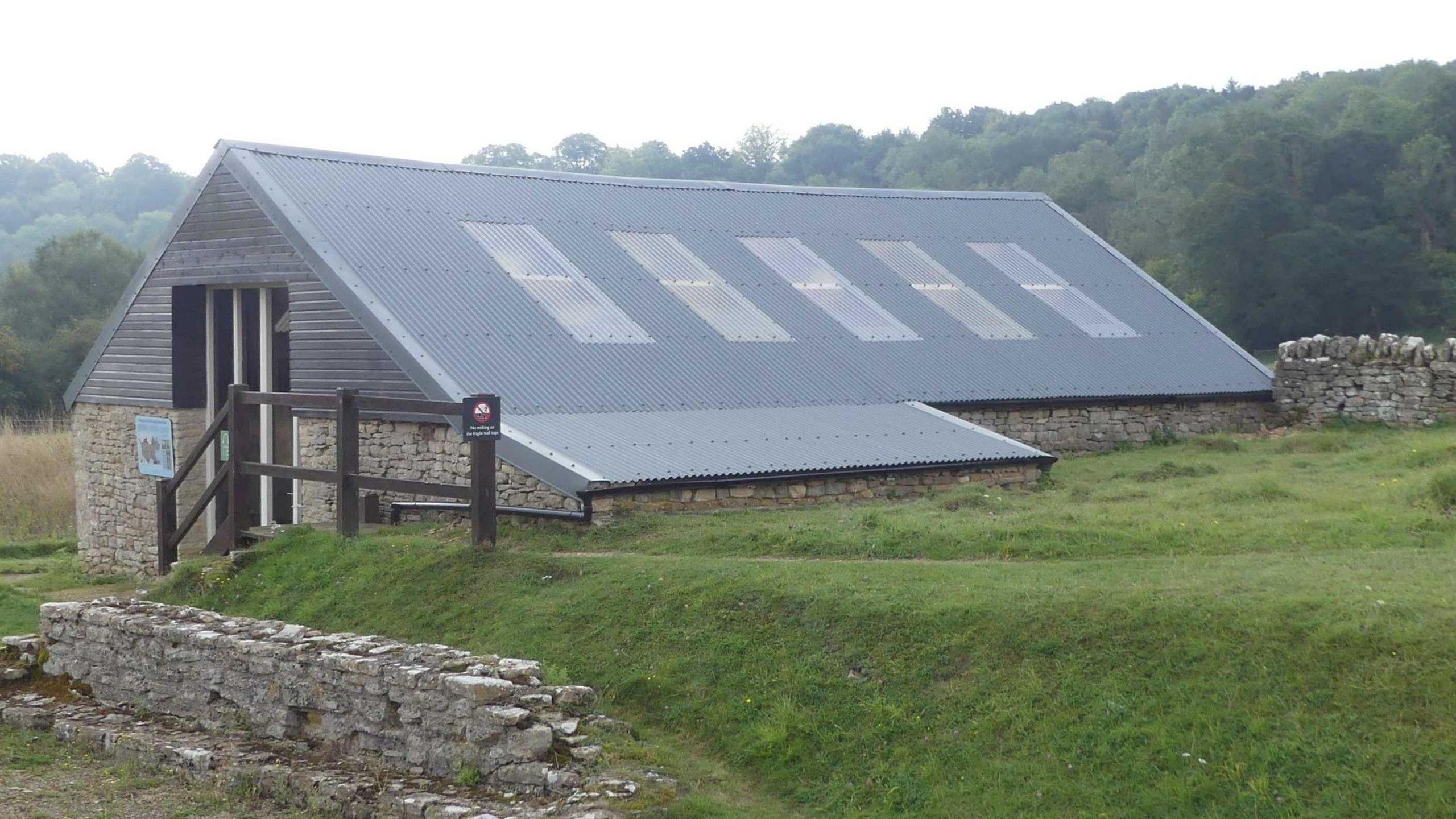 A stone building with a modern, wooden, grey roof and skylight windows.