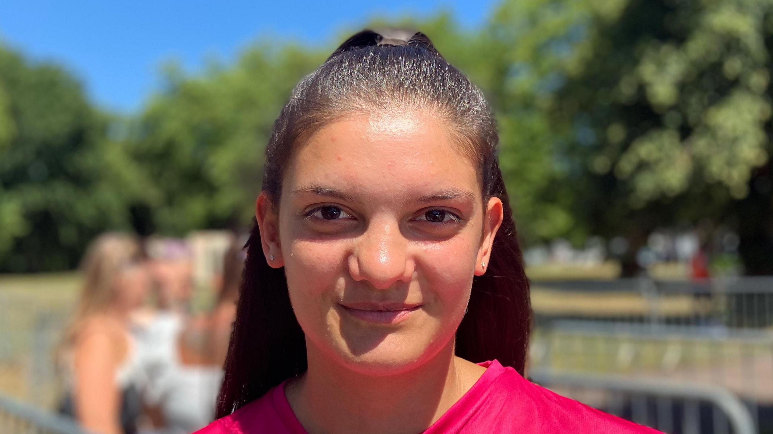 Mary Farruku smiles at the camera. She has long dark hair that has been tied back. She wears a pink Ipswich Town shirt.