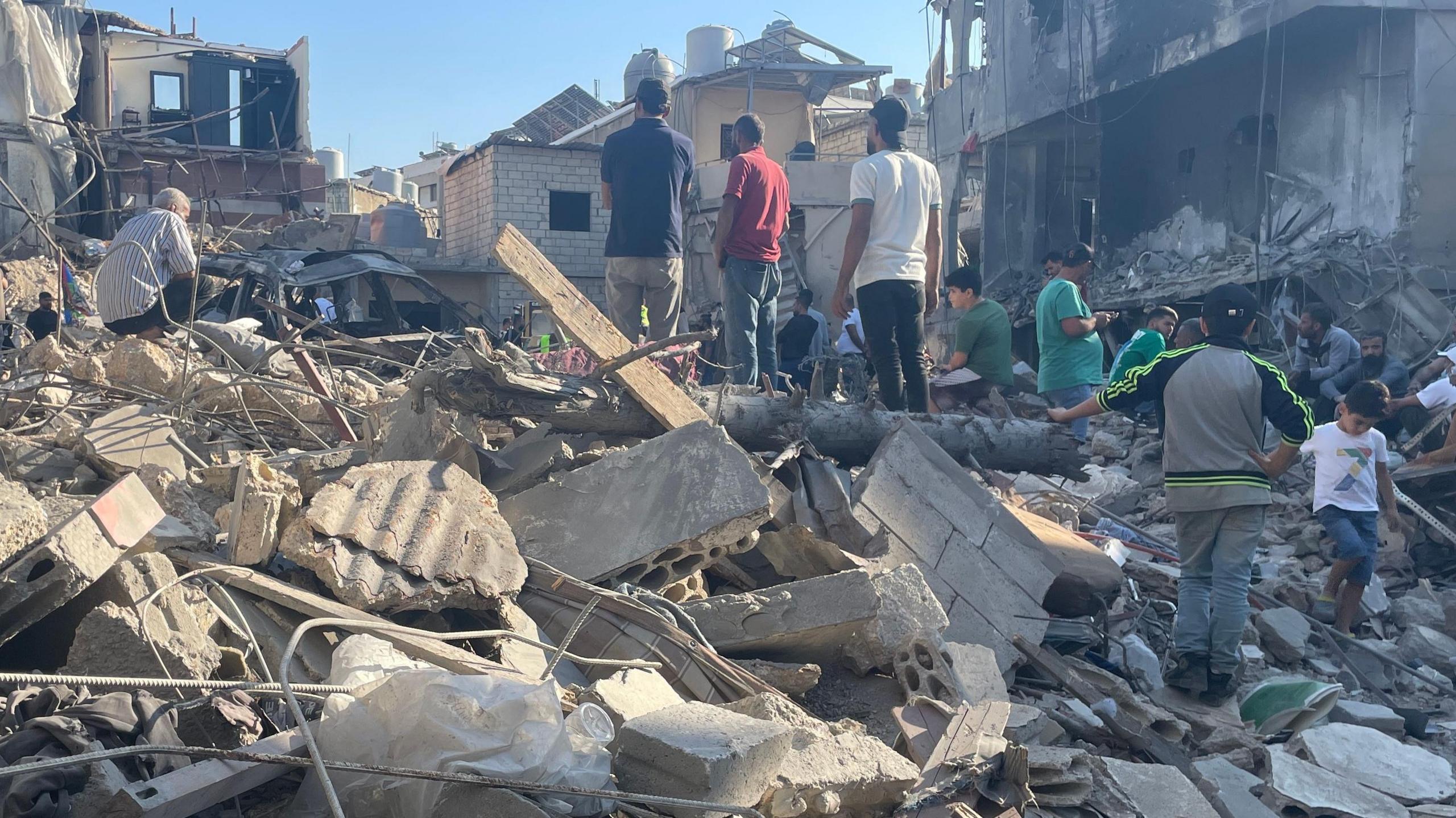 Groups of men stand on a mound of rubble and twisted metal after an Israeli airstrike hit a building. 