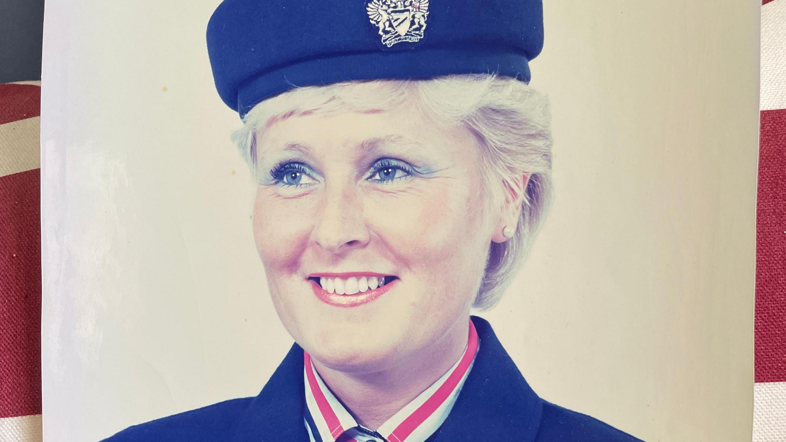 Image of Anne in her cabin crew uniform - a navy jacket with a matching hat. She has light blue eye shadow and red lipstick on. 