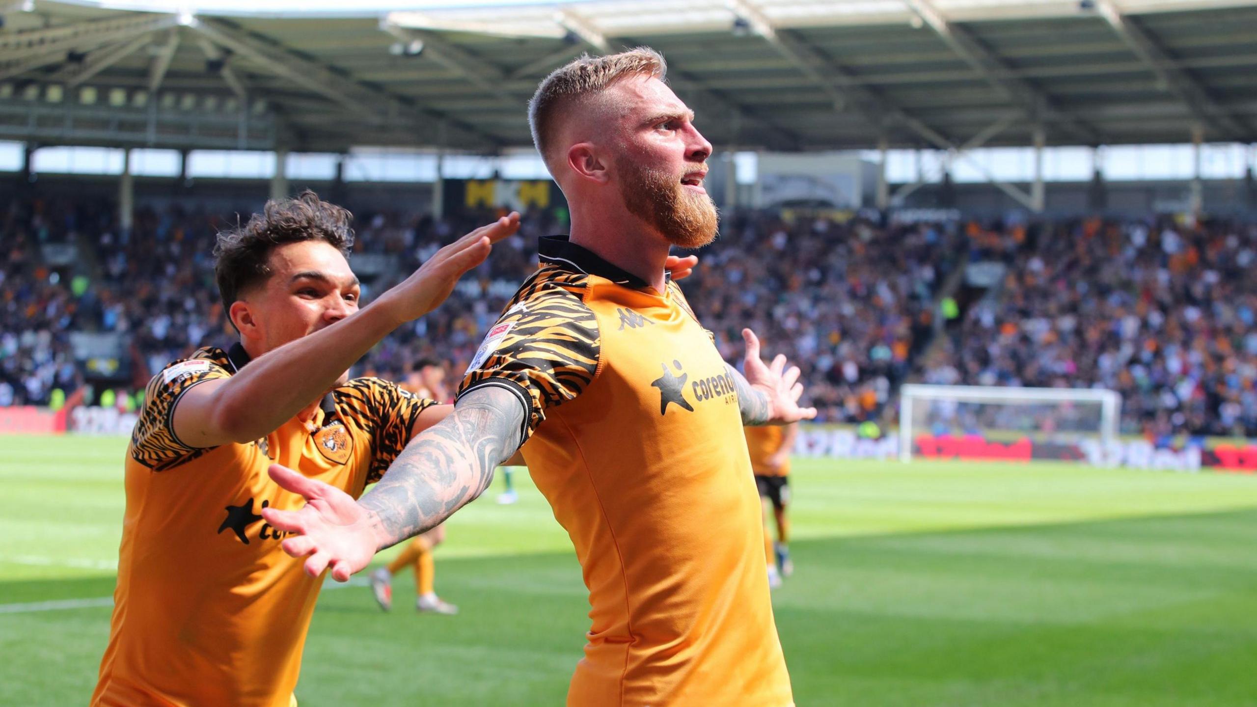 Oli McBurnie, wearing a Hull City home kit, celebrates his goal against Norwich City by holding out his arms while a team-mate runs behind him to congratulate him