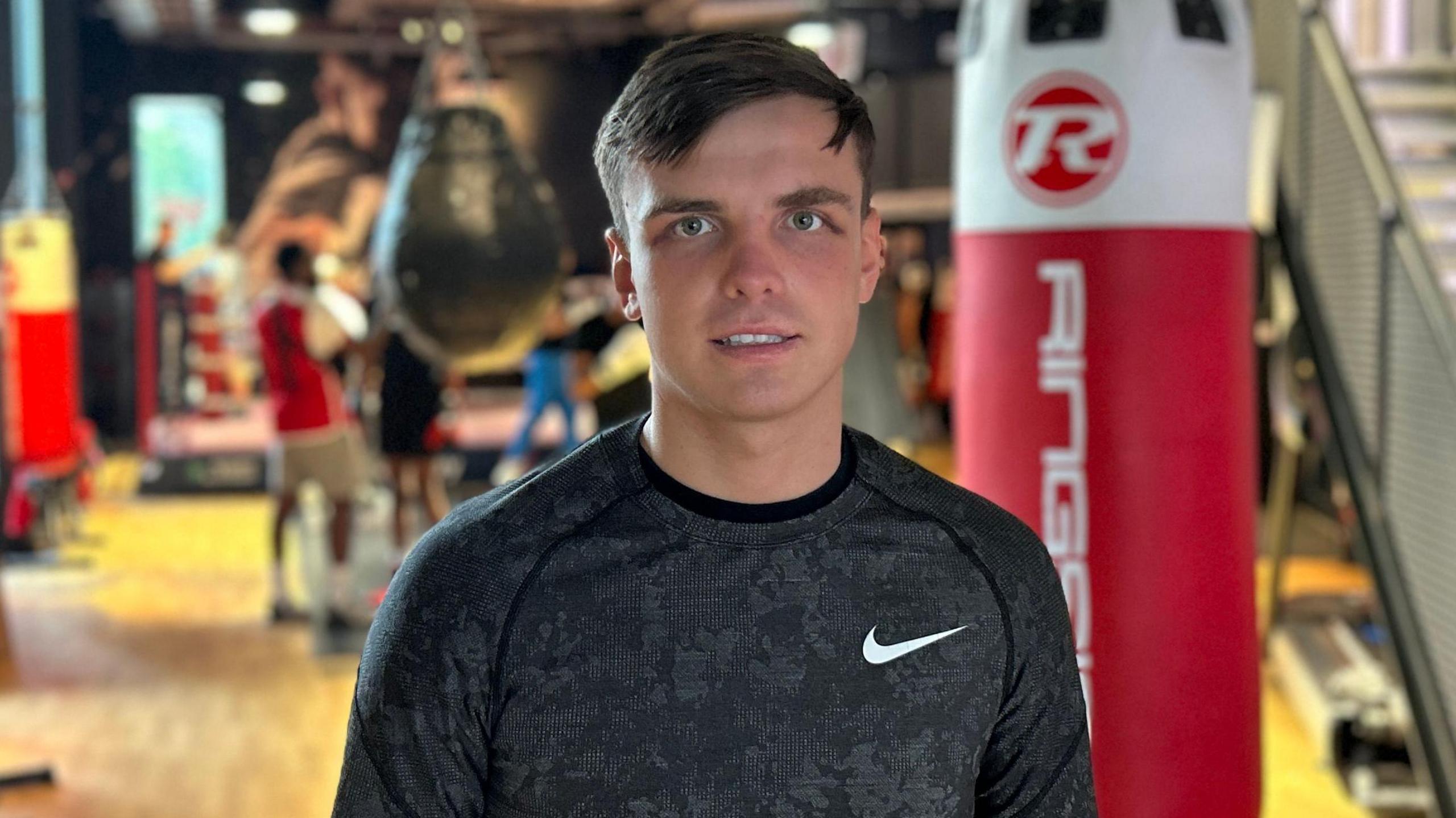 Tommy Murphy, a 23-year-old man with short brown hair and blue eyes, pictured wearing a Nike jumper standing in front of a boxing gym.