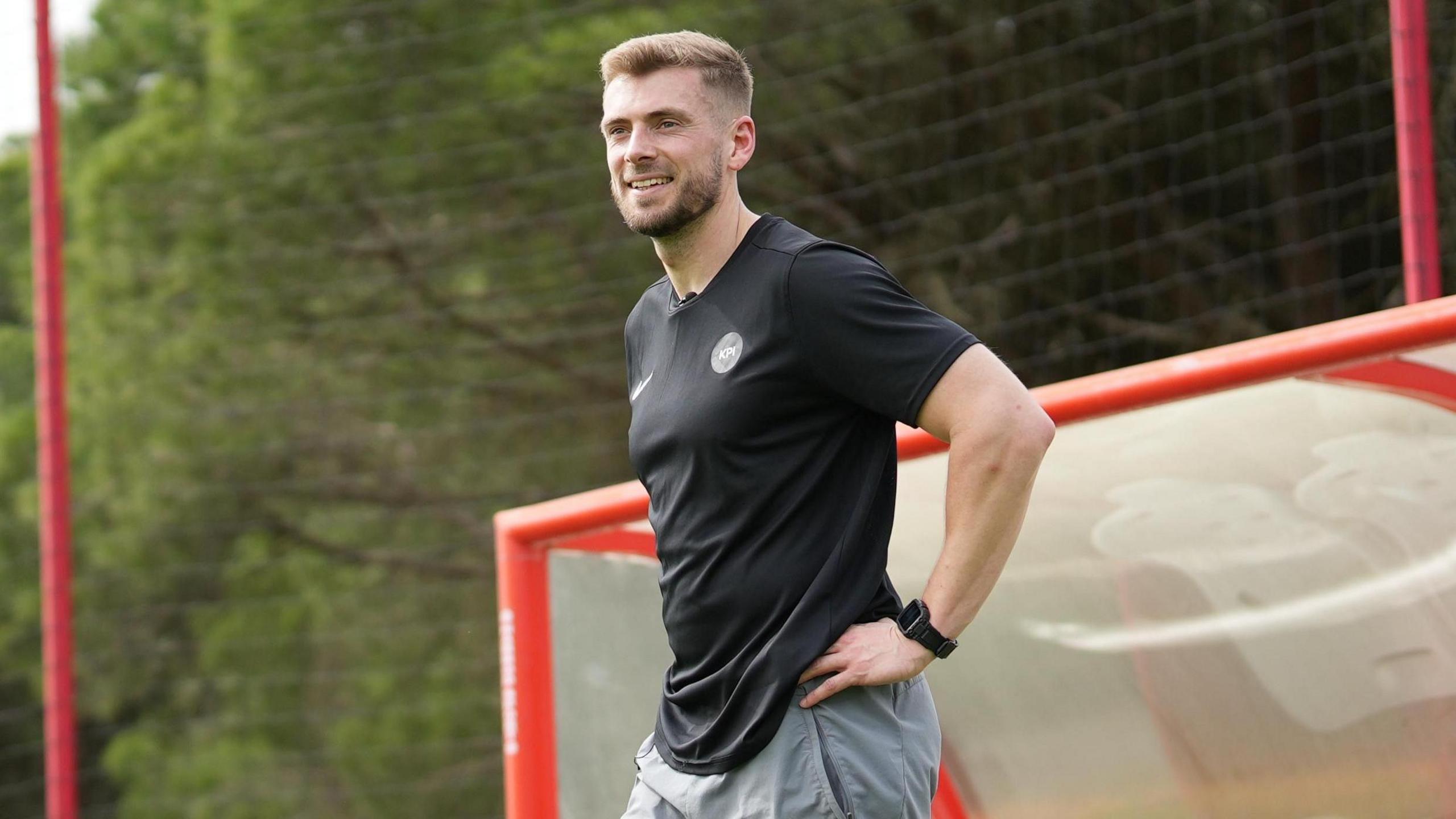Tom King poses in front of a dugout at a football ground