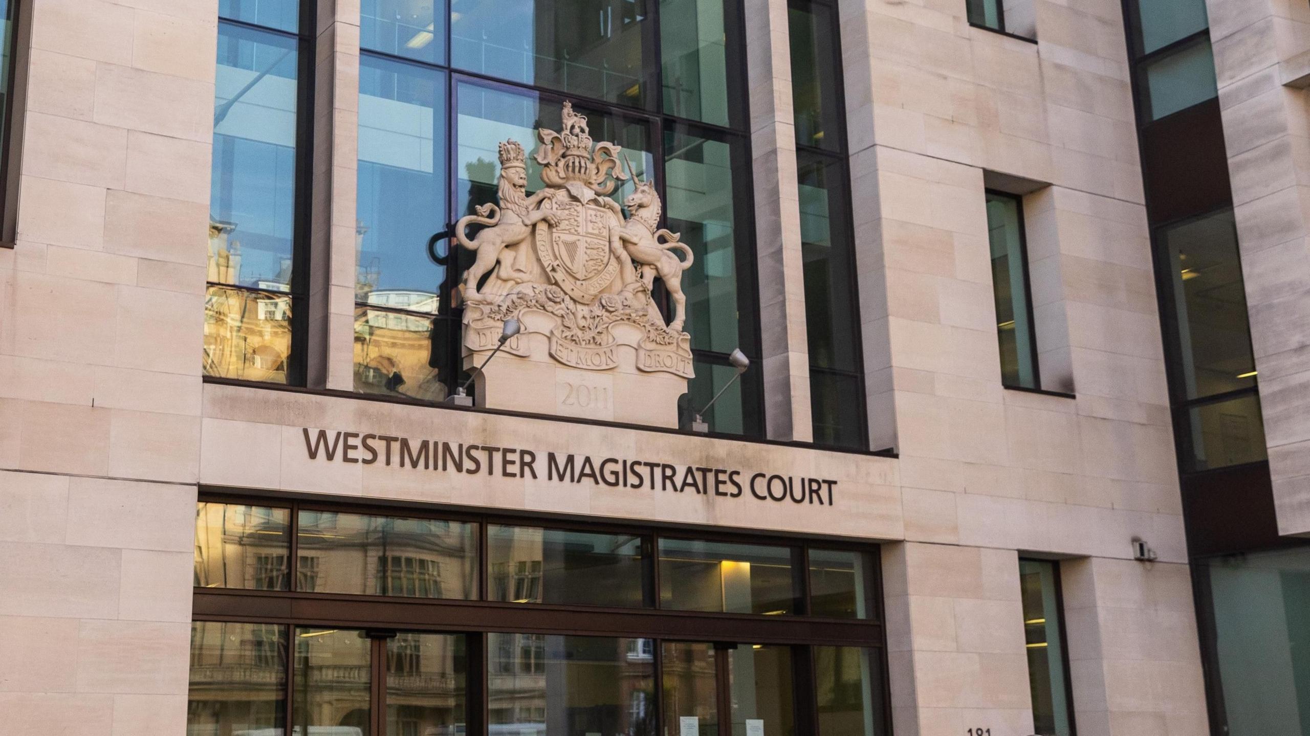 Westminster Magistrates Court from the outside. The words and crest of the court are displayed about glass doors and windows.