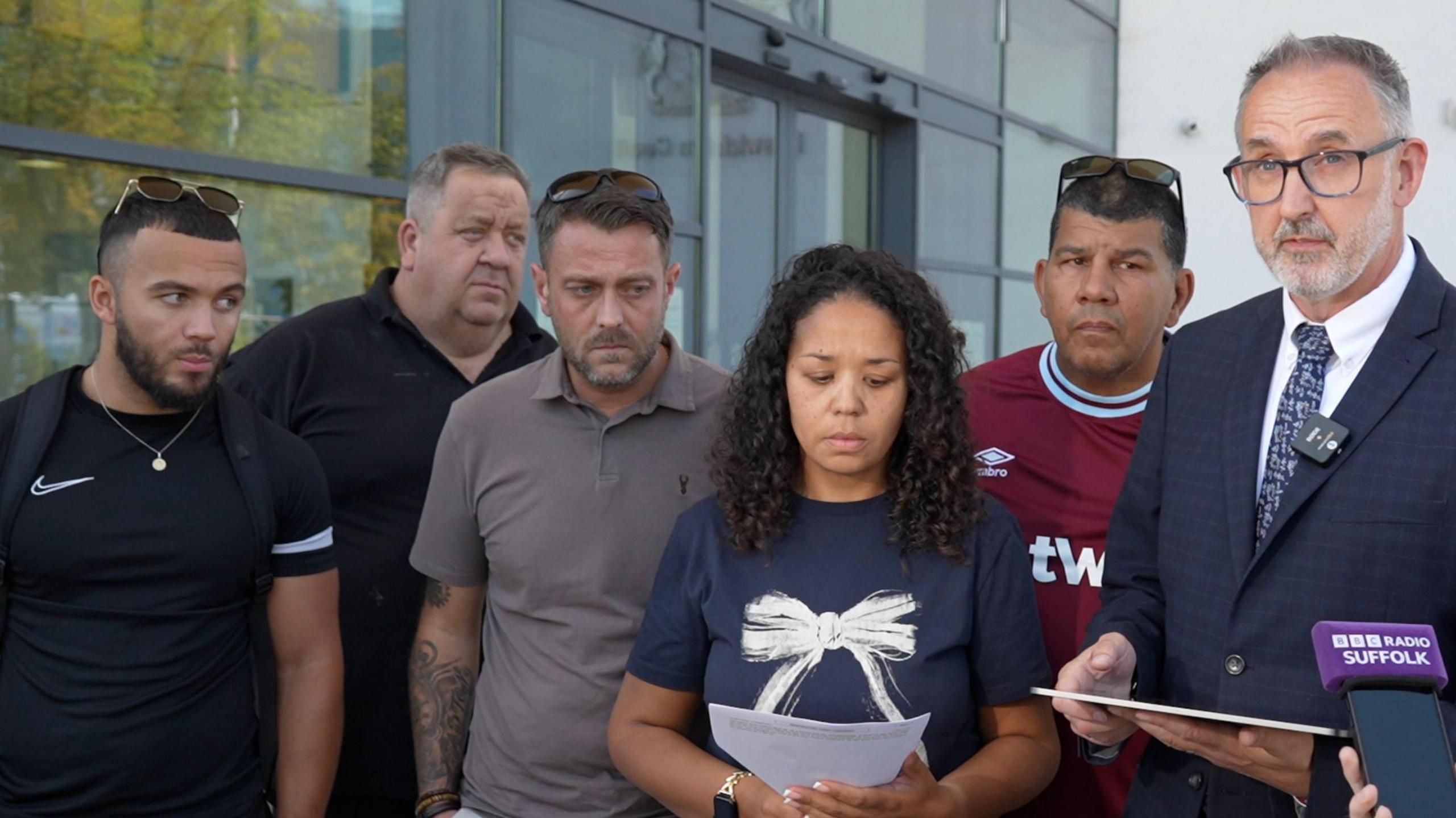 Anita Rose's family stand in a group outside Ipswich Crown Court. Her daughter Jess holds a piece of paper with her statement on it and she looks down at it.