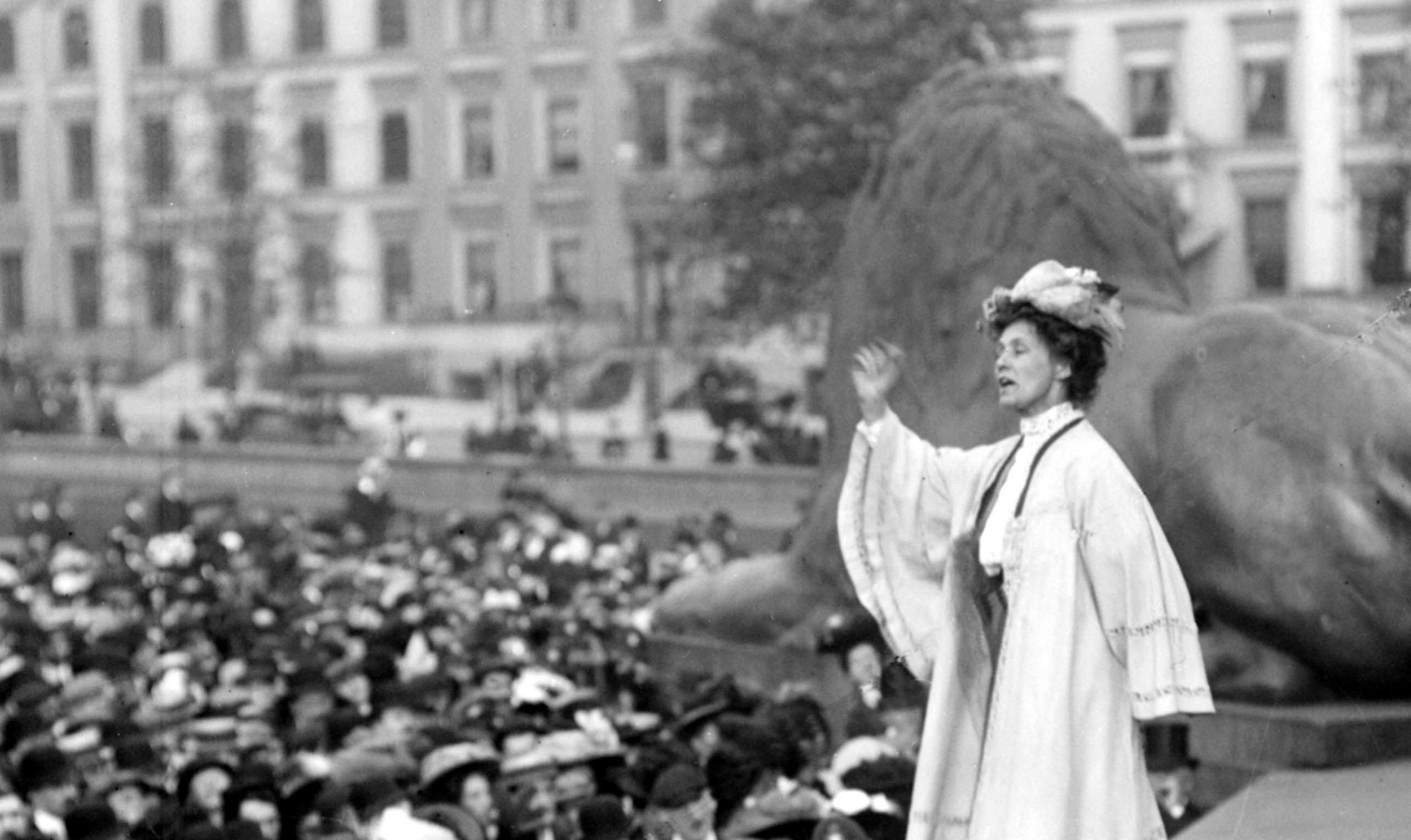 Suffragette Emily Pankhurst addressing a meeting in London's Trafalgar Square. In the black and white photograph, she is standing with her right arm up, eyes closed while a crowd look up at her