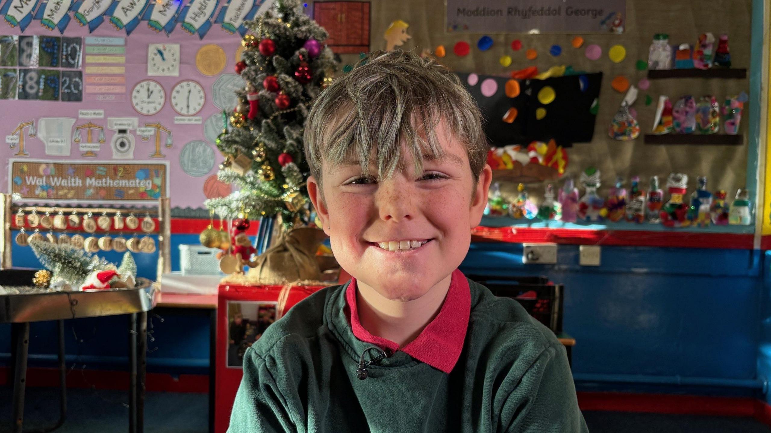 Efan smiles. His hair is ruffled and he is wearing a green jumper  