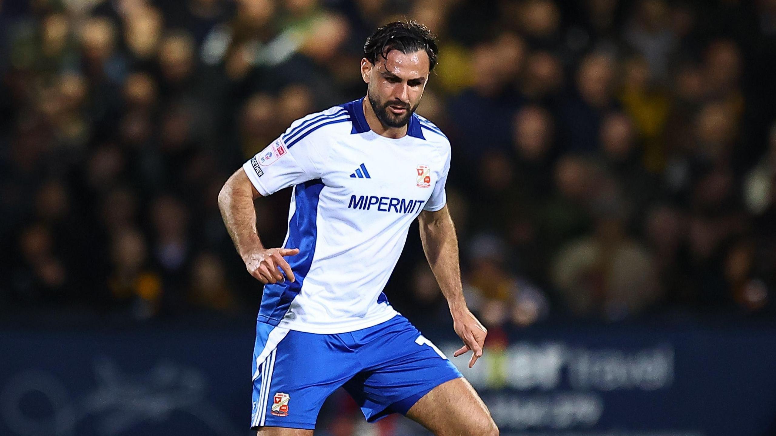 Ryan Tafazolli wearing Swindon's away kit of a white shirt and blue shorts is captured during Swindon's win against Walsall.