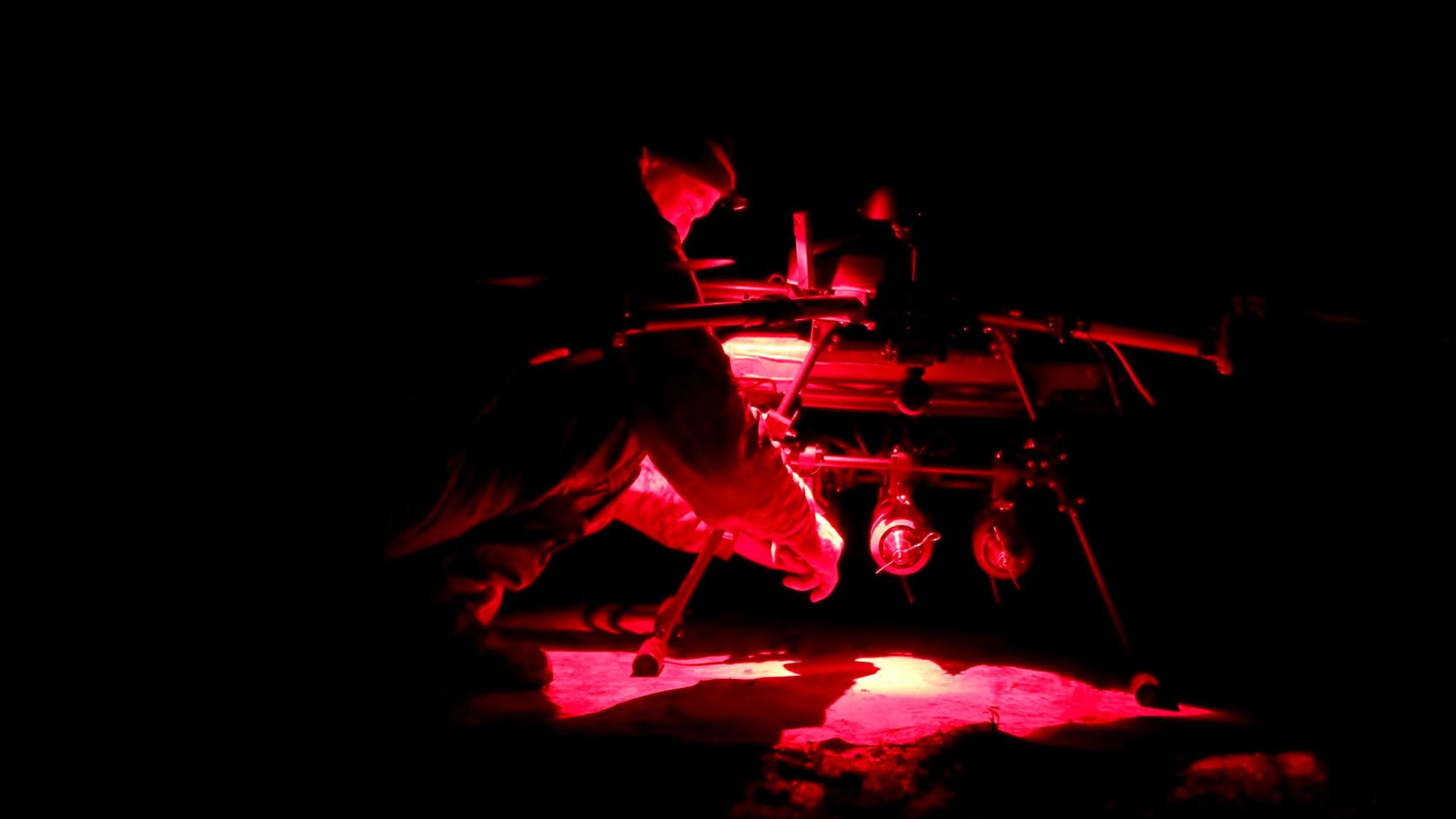 Man adjusts a vampire drone cast in red light outside in the dark