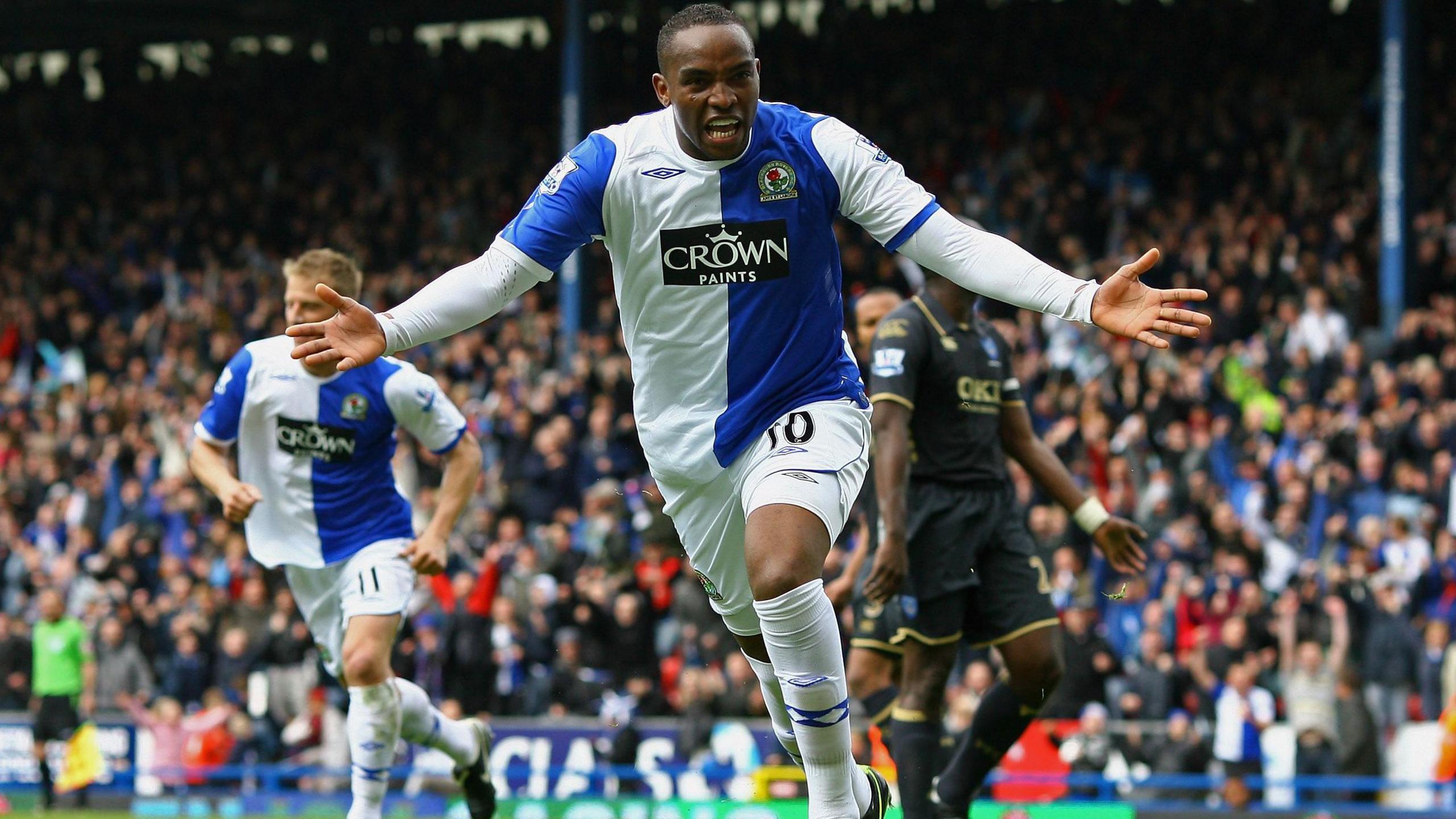 Benni McCarthy in blue and white Blackburn Rovers shirt wheels away and spreads his arms wide in celebration after scoring a penalty in a Premier League game at Ewood Park.