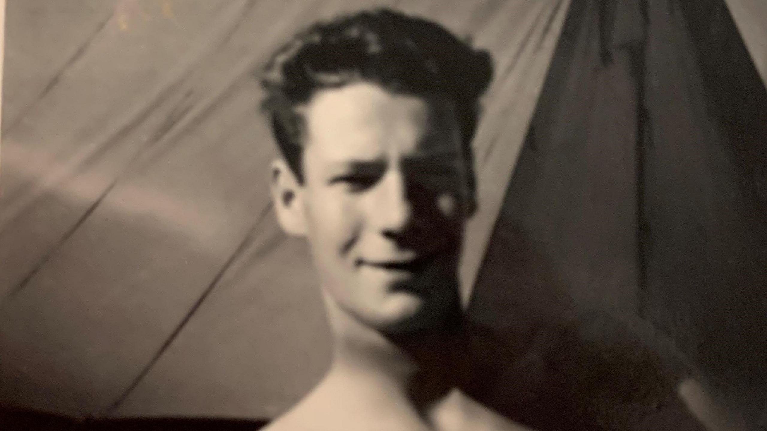 A blurry photo shows a young Robert James, with wavy dark hair, standing bare-chested near a tent