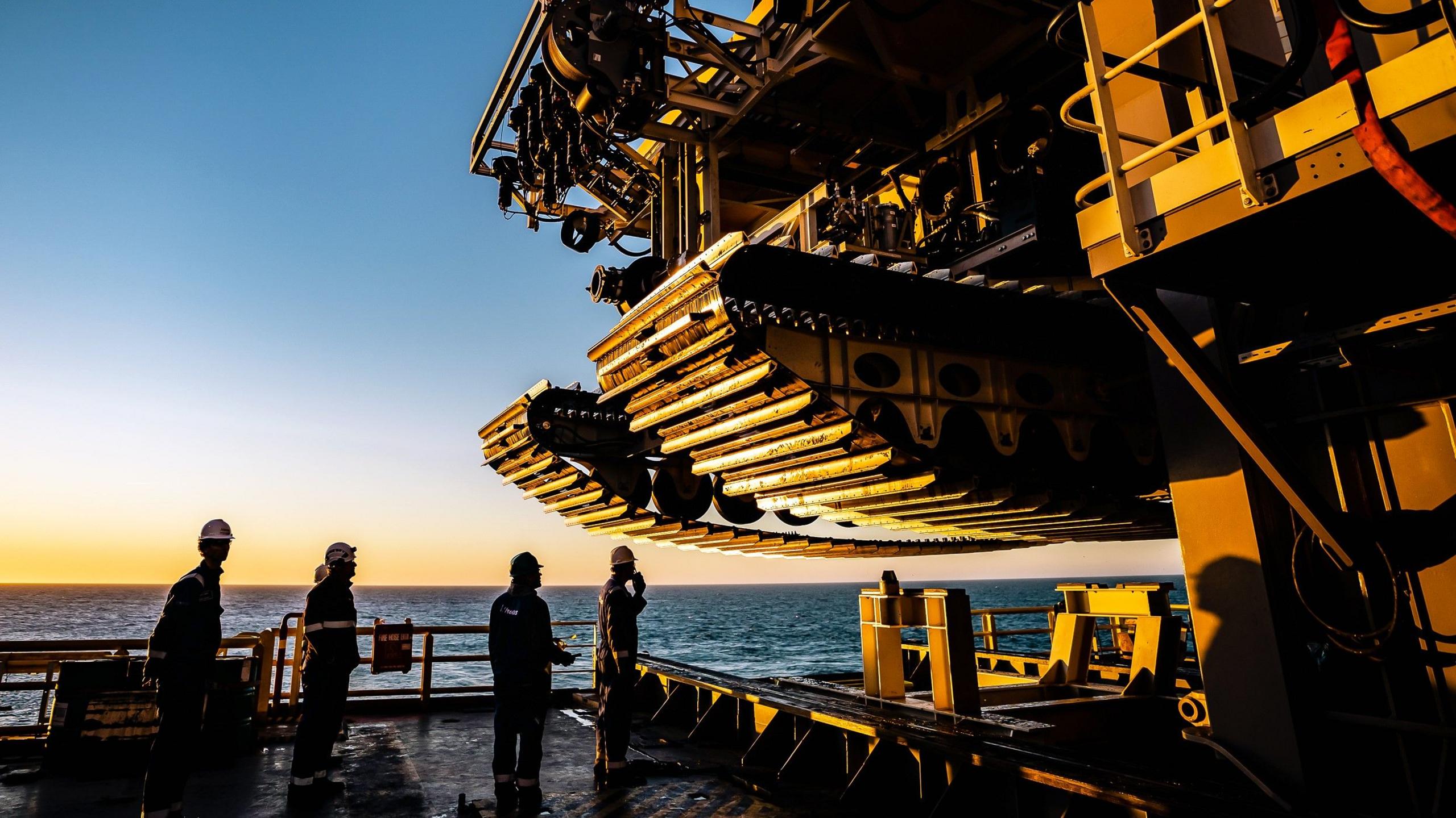 The crew of a ship look up at the tracks of a subsea mining vehicle.