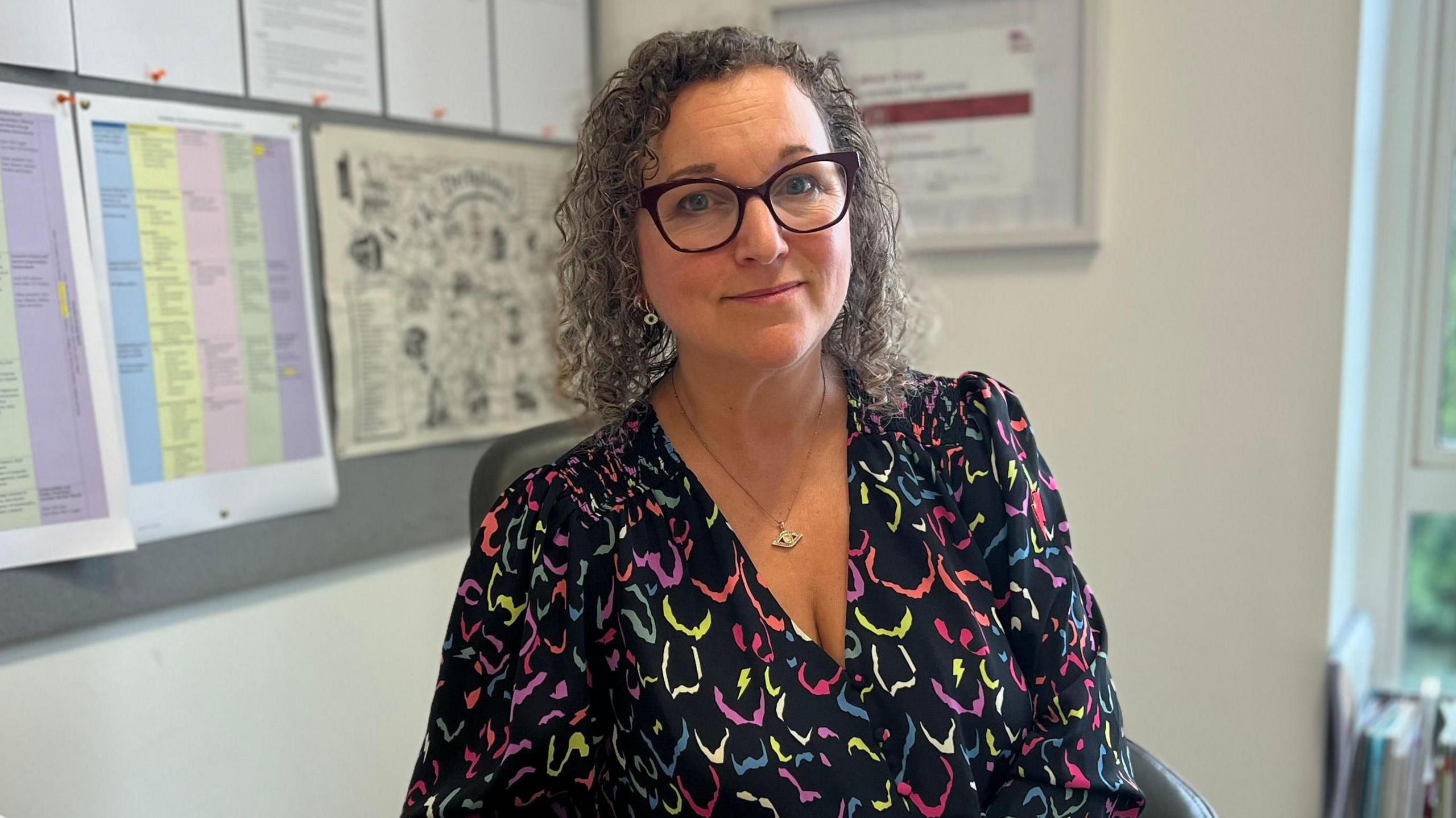 Image of Nadine. She has shoulder length dark hair and is wearing glasses.