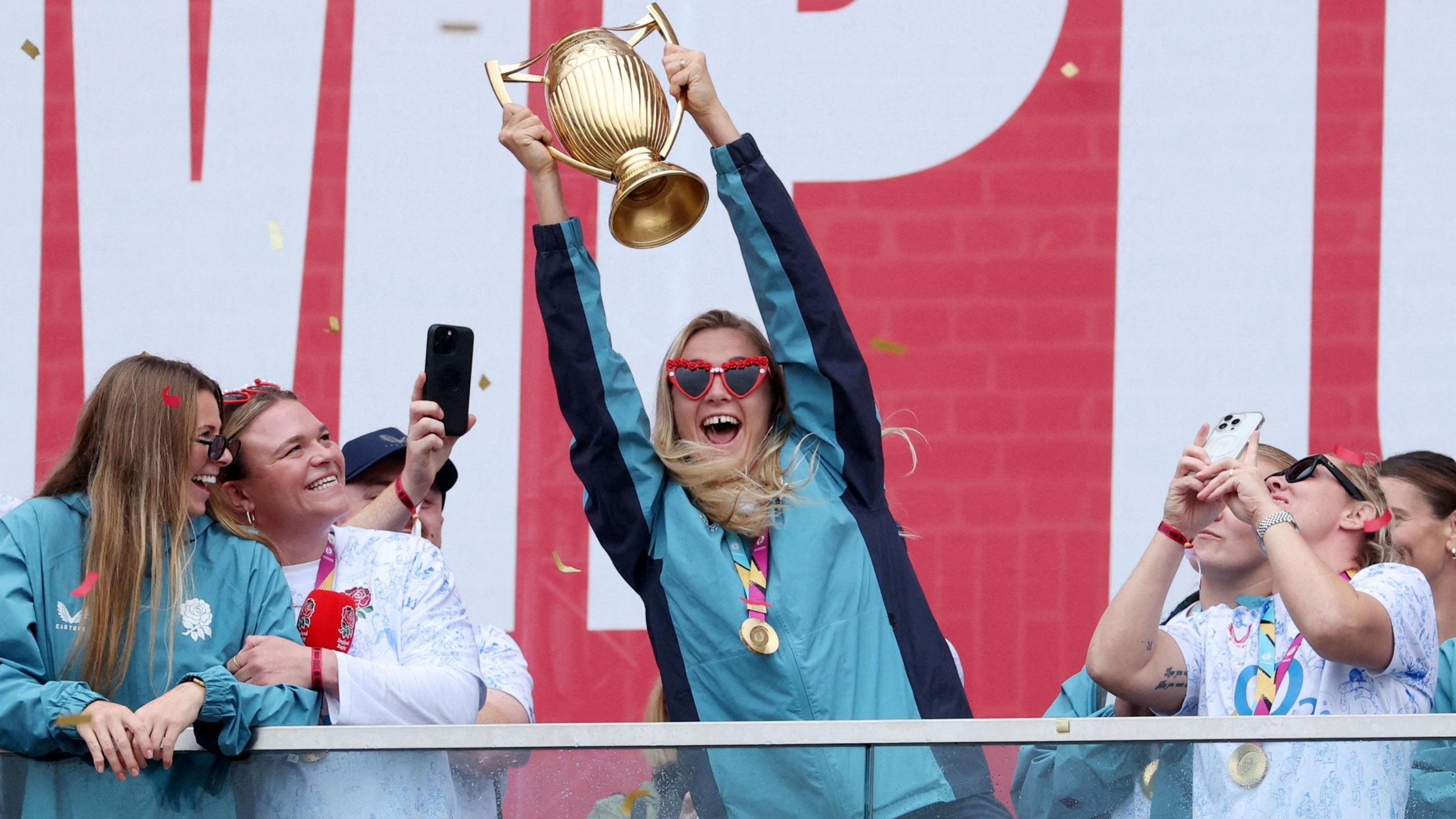 England's Zoe Aldcroft lifts the trophy as she celebrates with her teammates during their champions party 