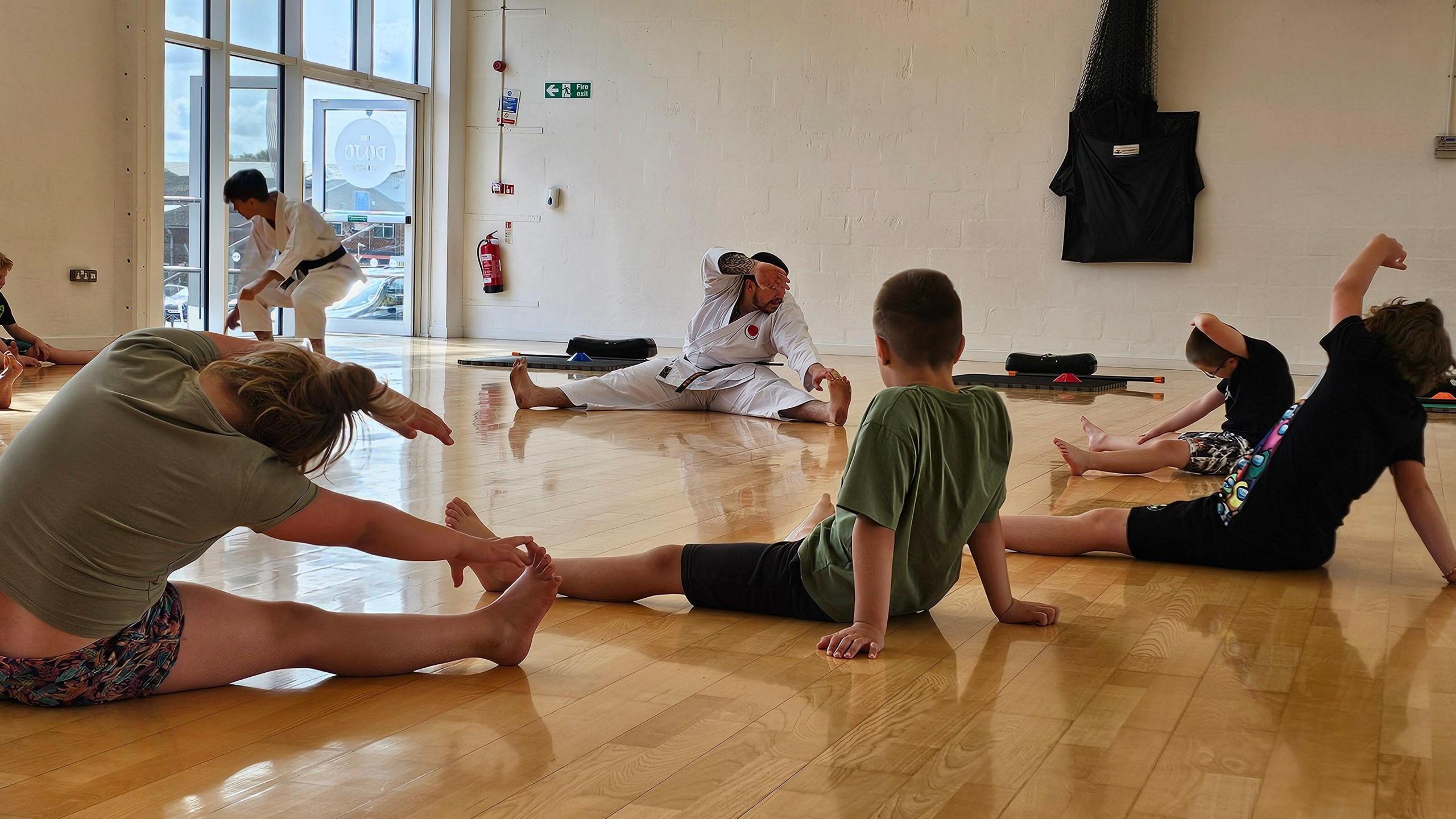 A karate instructor stretching whilst teaching a group of children.