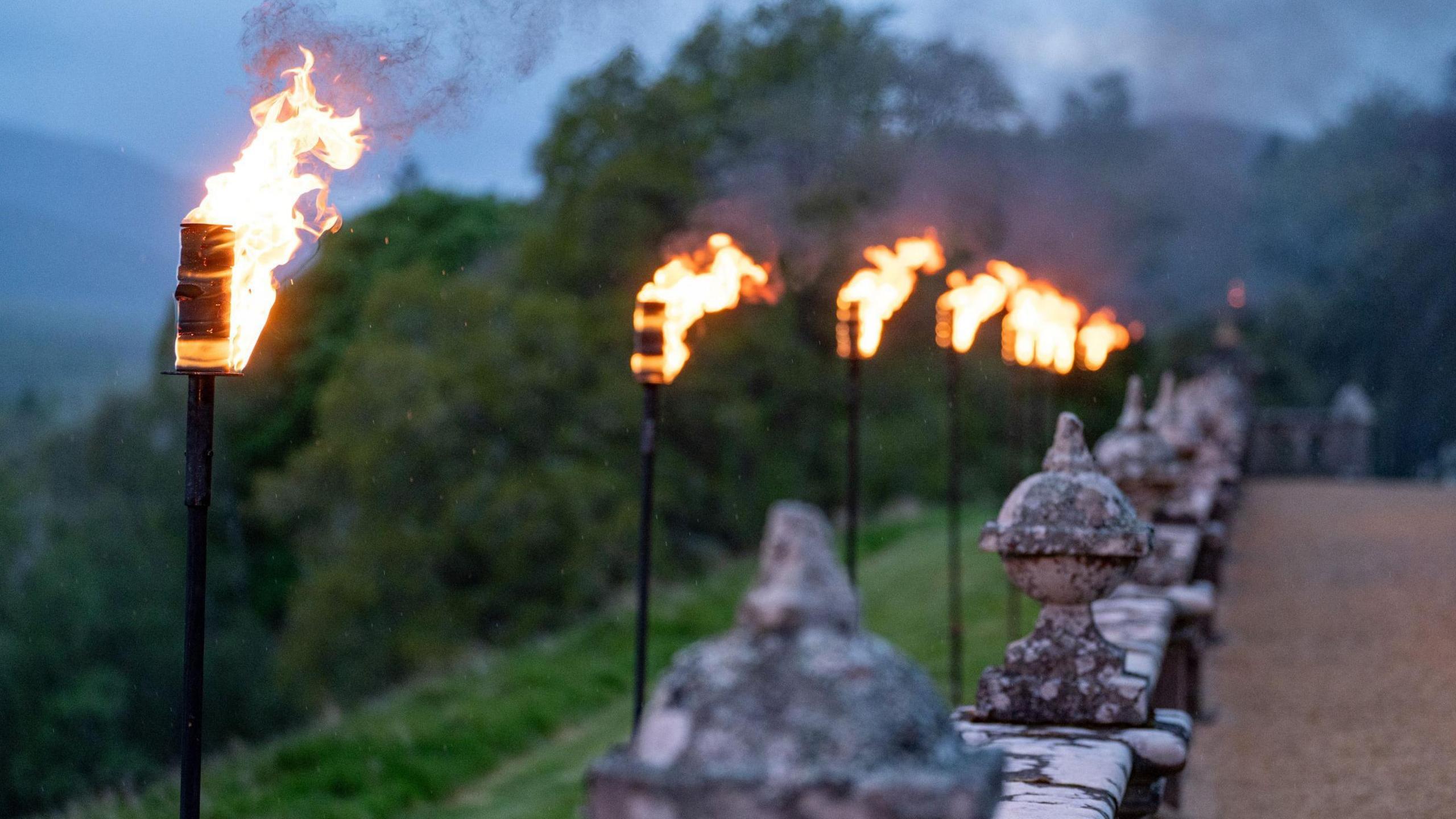 Flaming lanterns lead the way along a stone wall at the castle. 