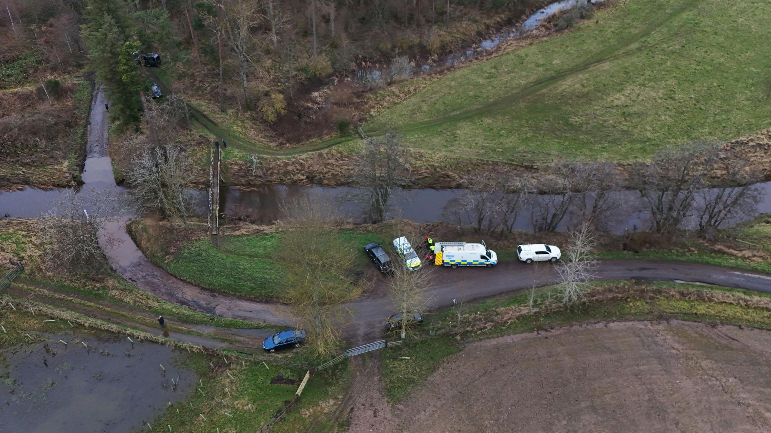 An aerial shot of Abberwick Ford where a very rural road crosses the river Aln. Five vehicles including two police vehicles are parked up.