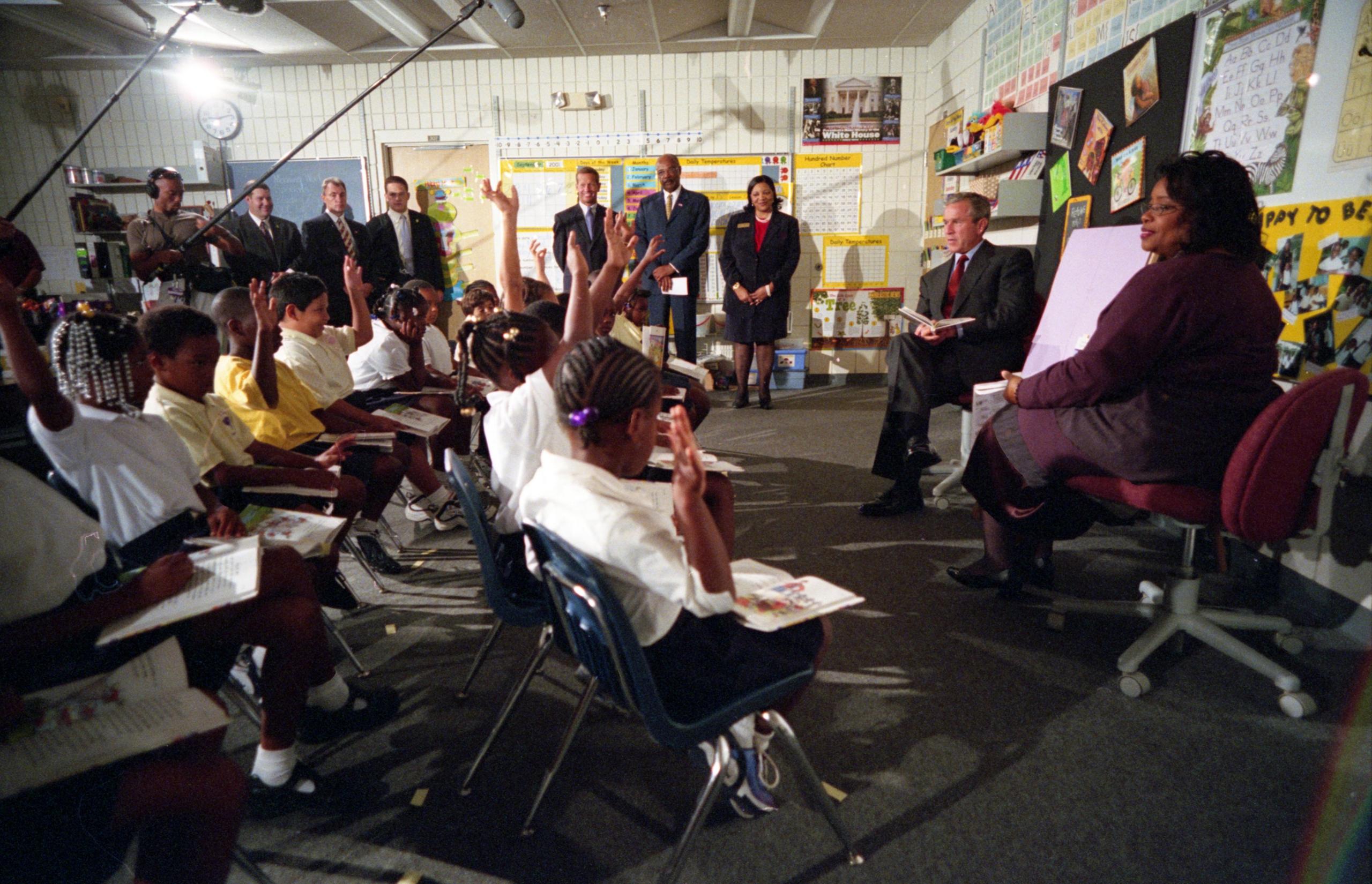 Class of Booker School have their hands up while President Bush sits in front of them.