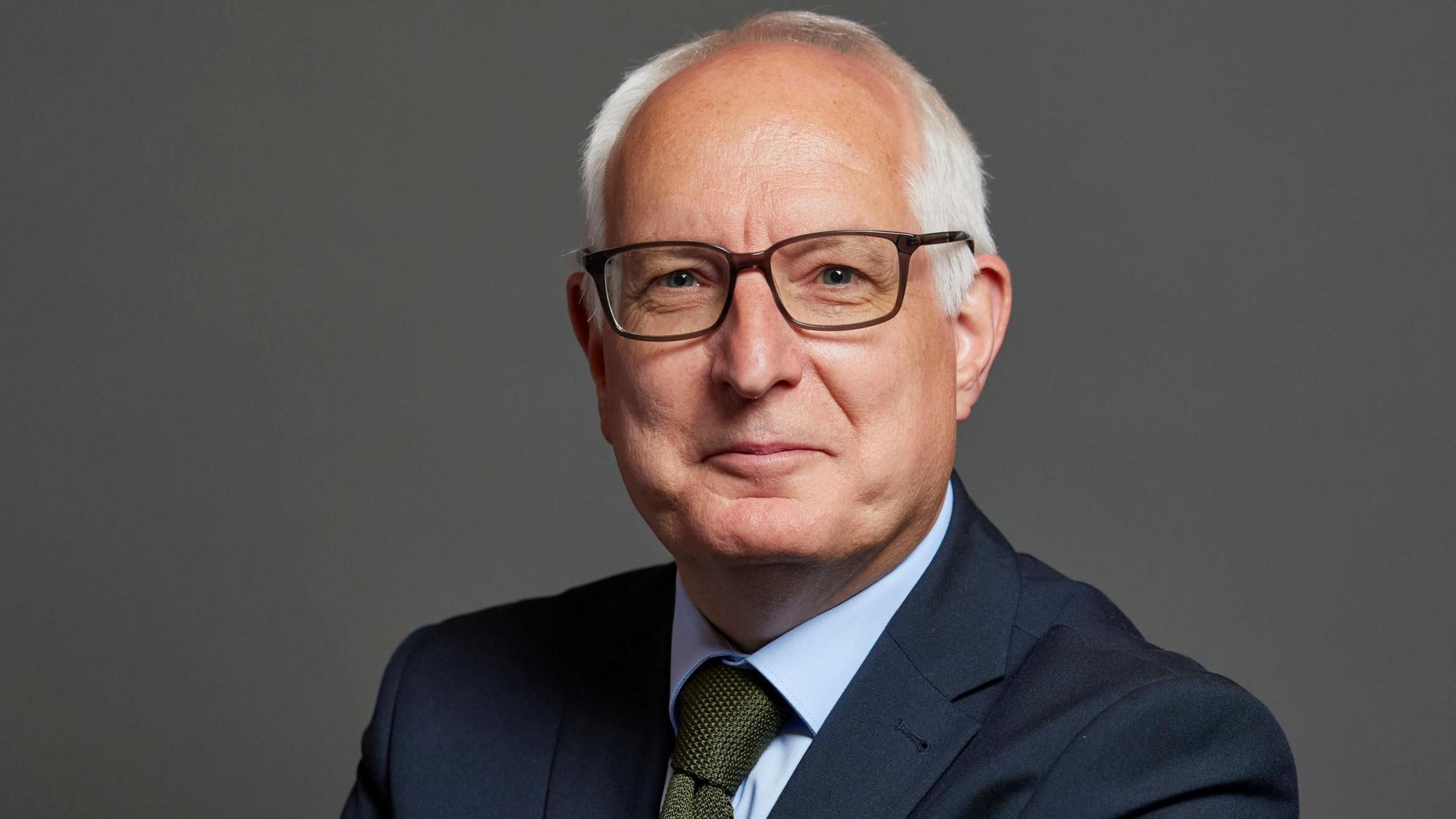 Neil Duncan-Jordan who is looking directly at the camera and smiling. He is wearing a navy suit jacket with a pale blue shirt and green tie.