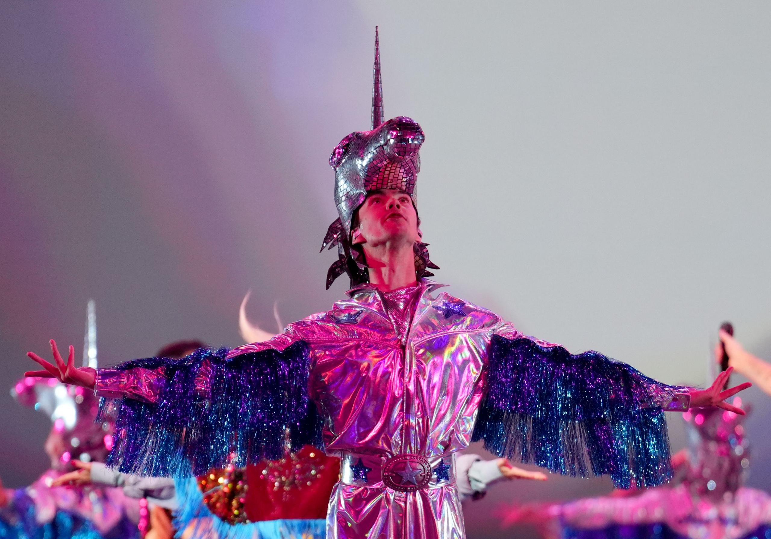 A dancer wearing a silver suit and a glitter unicorn headdress dances on stage.