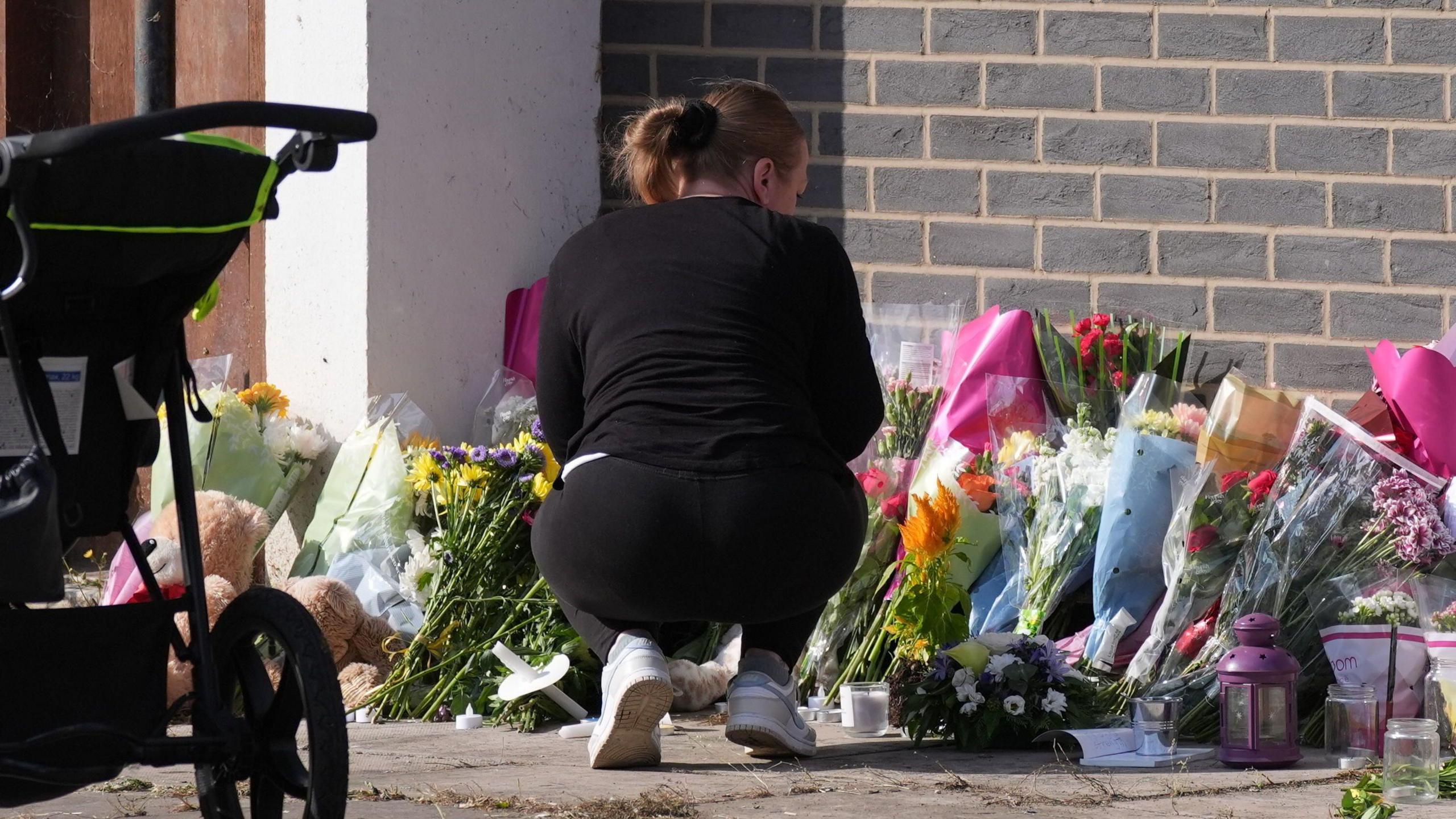 A woman dressed in black bends down to look at the flowers, with a pushchair nearby