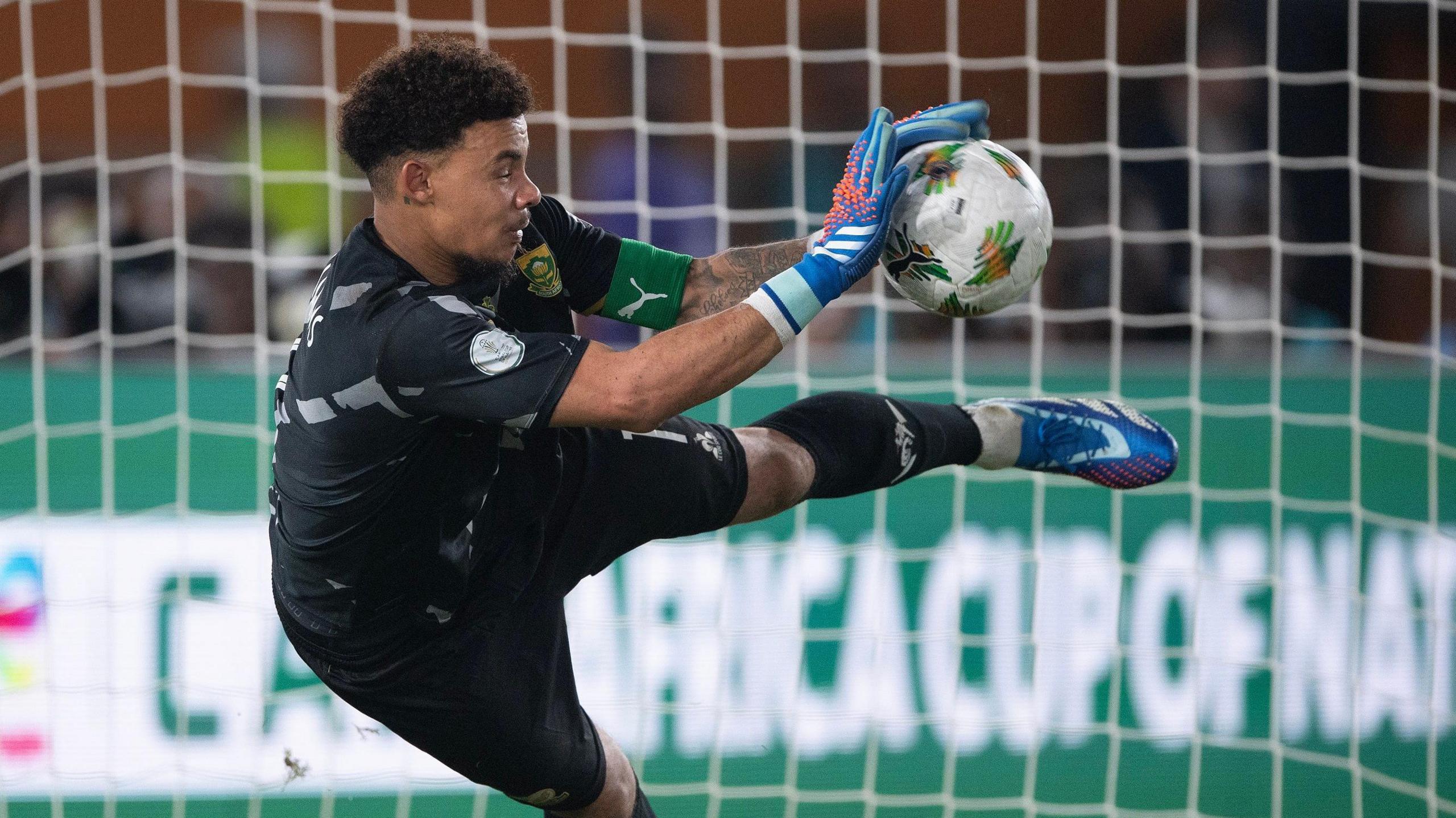 Ronwen Williams dives to his right to palm away a football during a penalty shootout at the 2023 Africa Cup of Nations