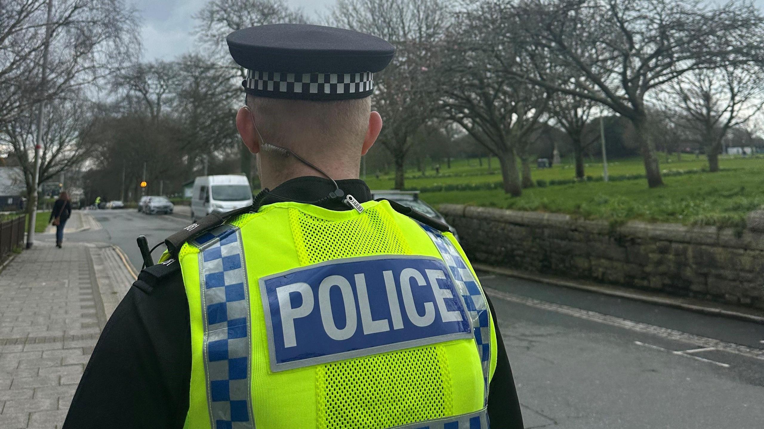 An anonymous police officer in a hi-visibility vest, walking along a street