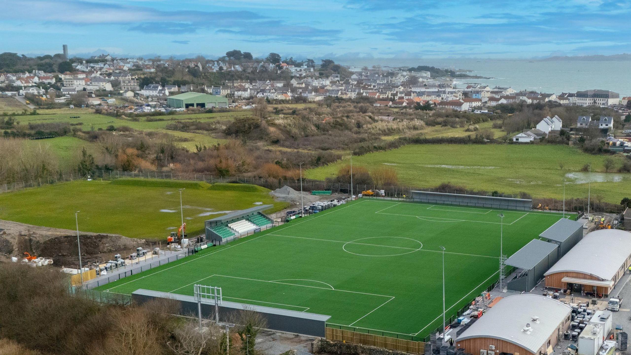 An aerial photo taken on a bright day showing Victoria Park, surrounding fields, the neighbouring town and the bay beyond. 