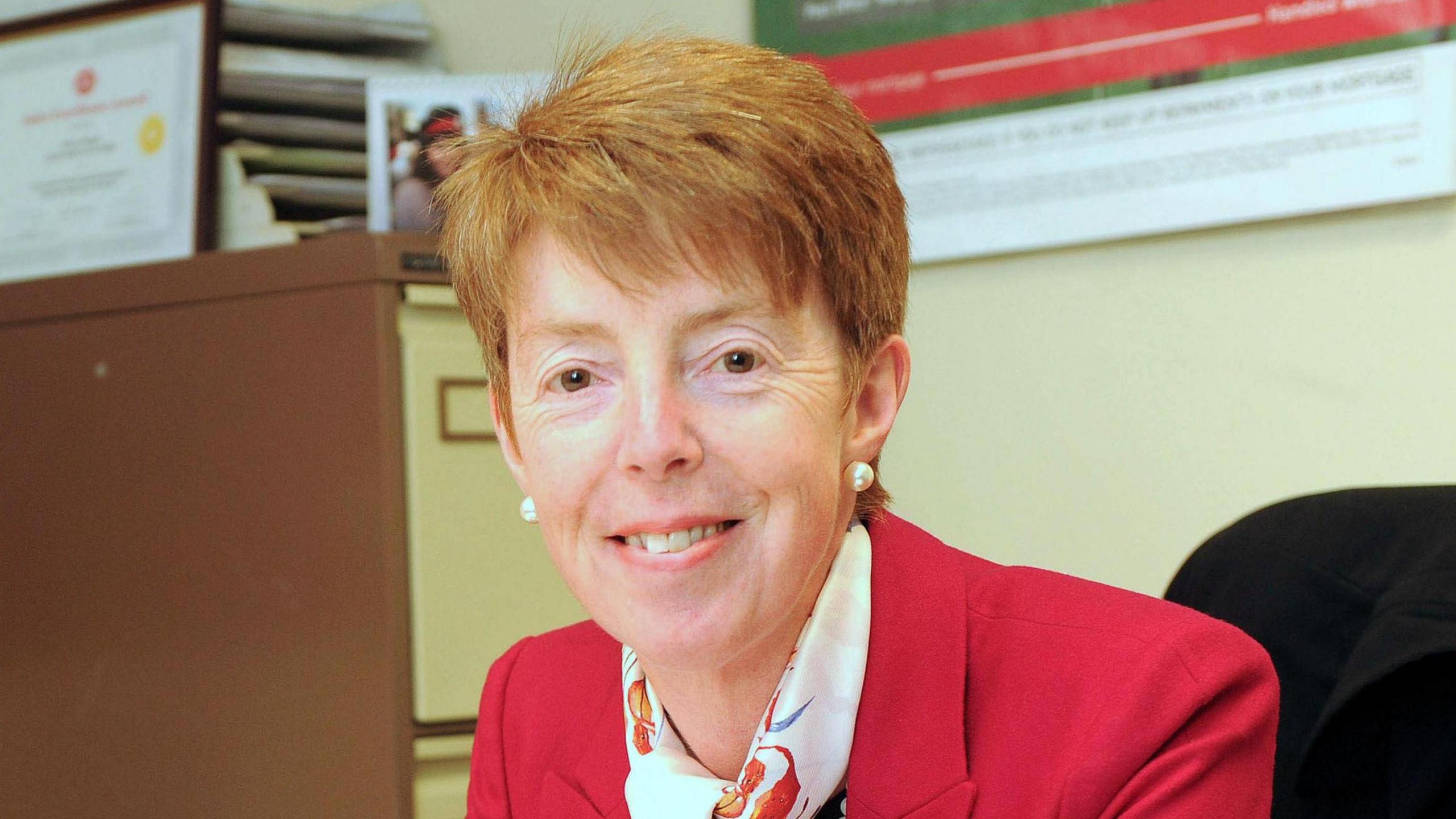 Former Post Office boss Paula Vennells sits in an office at a desk smiling at the camera