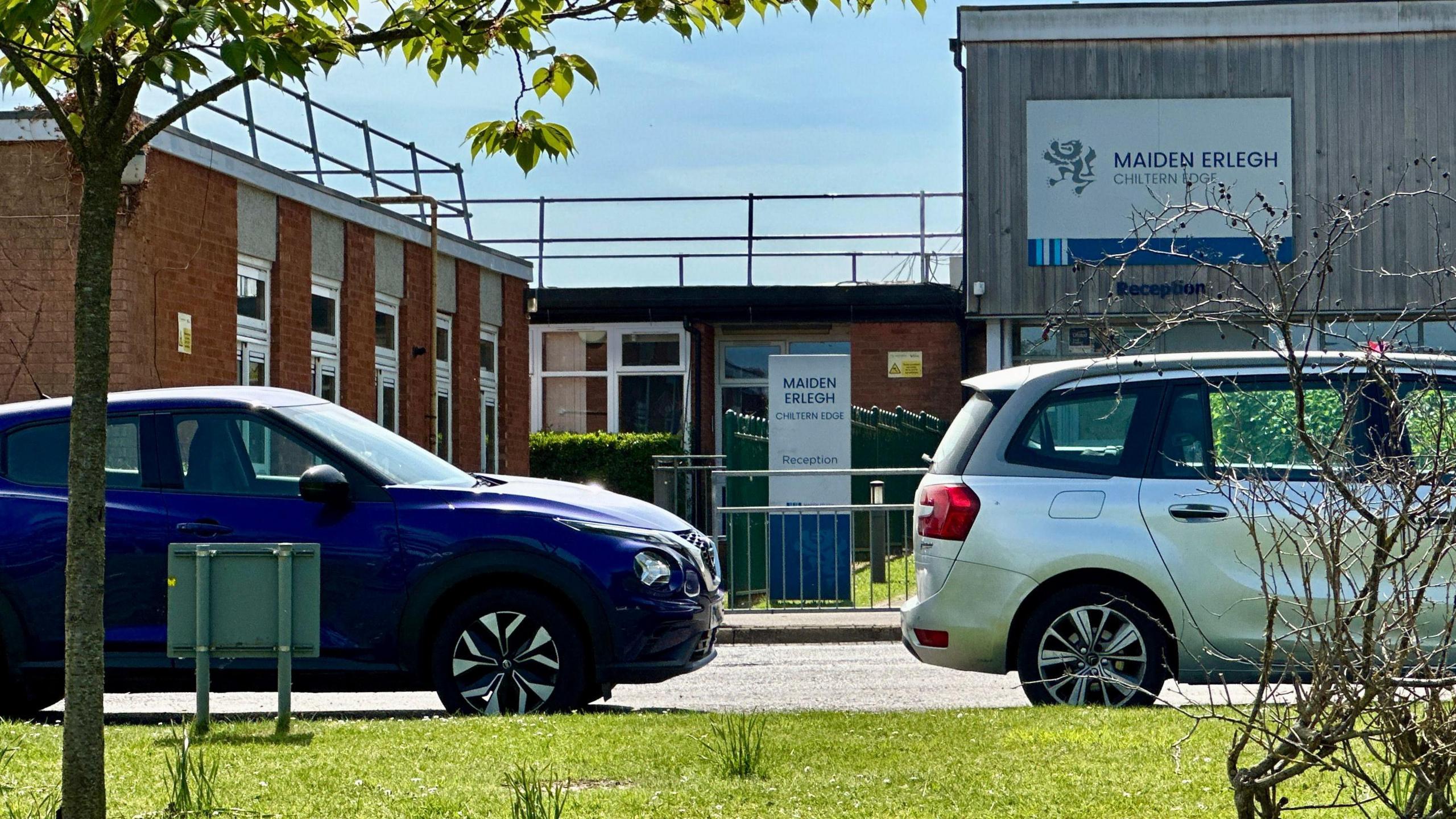The exterior of Maiden Erlegh Chiltern Edge school pictured in the sunshine with two car parked outside.