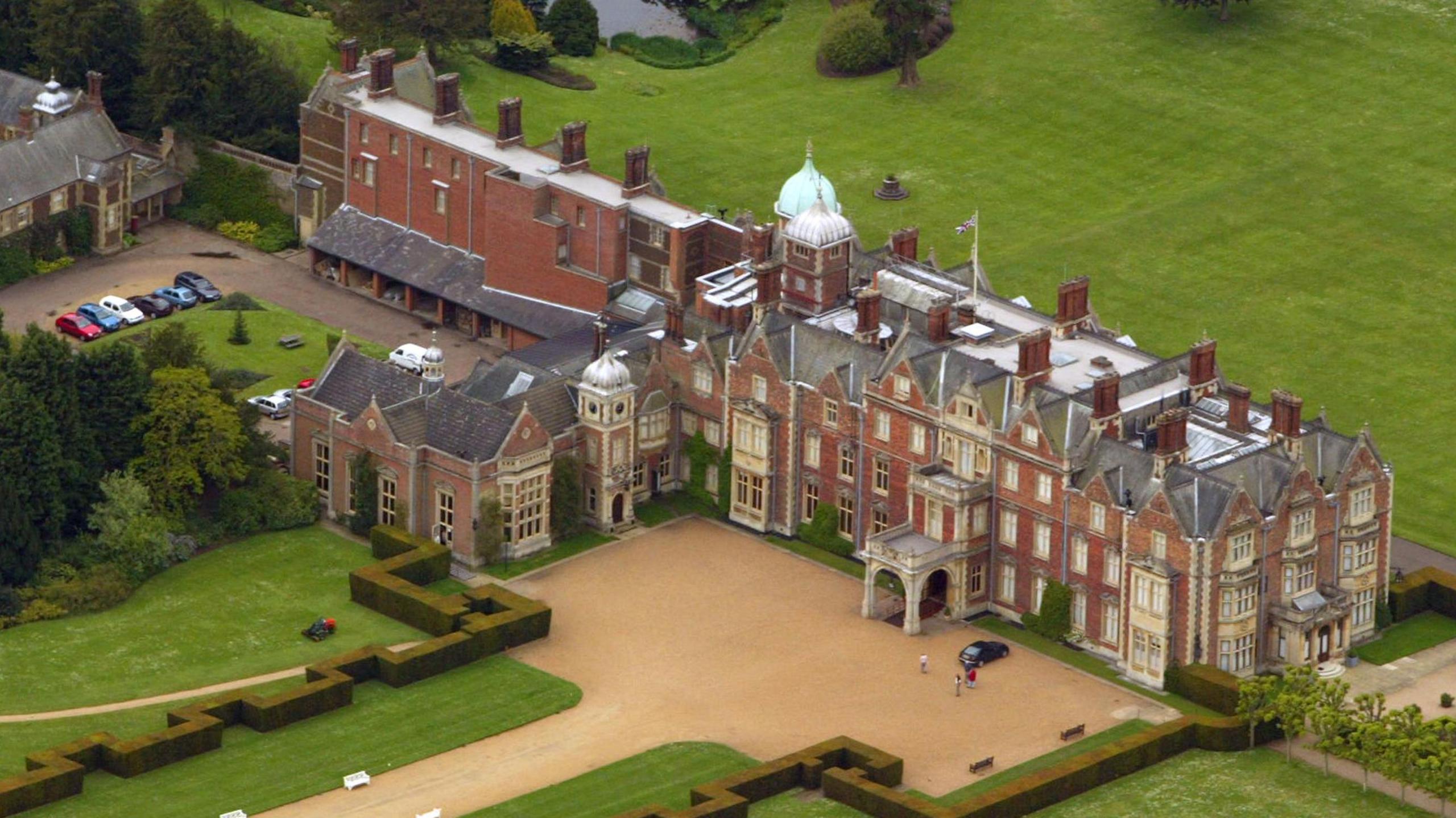 An aerial of the Sandringham Estate in Norfolk. The house sits on a lawn of green grass and a gravelled driveway. 