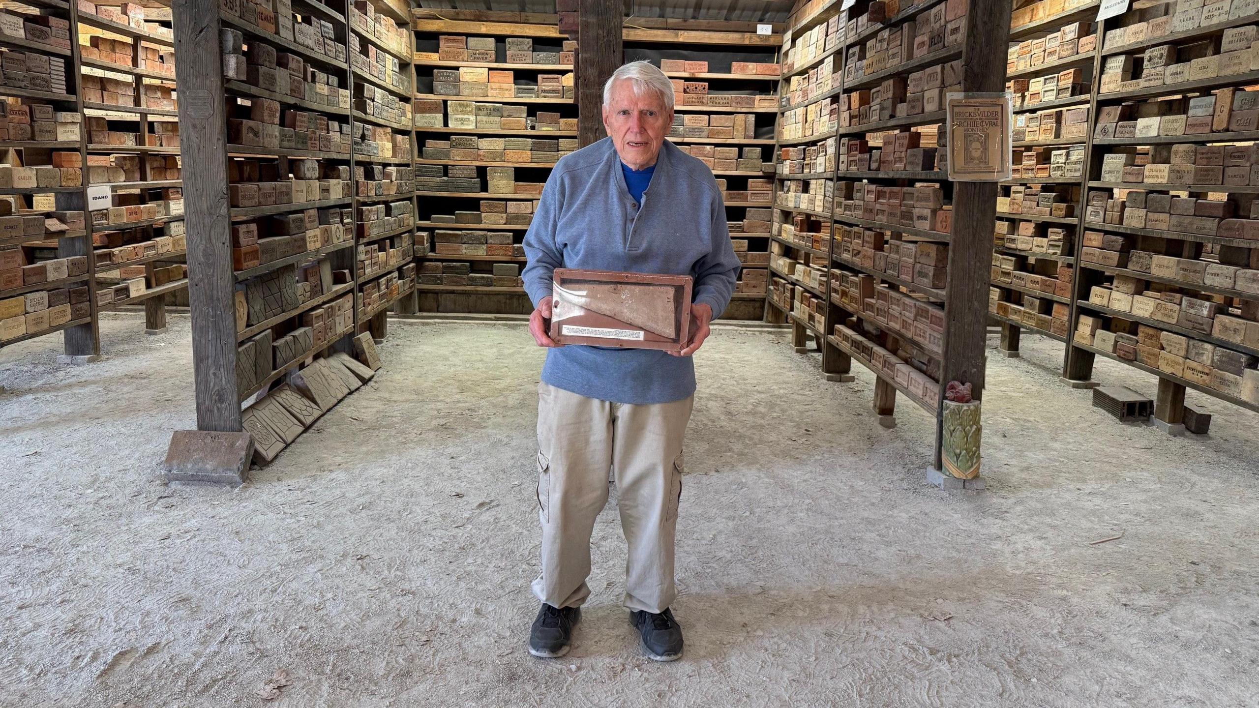 Clem holding a brick in his barn full of bricks