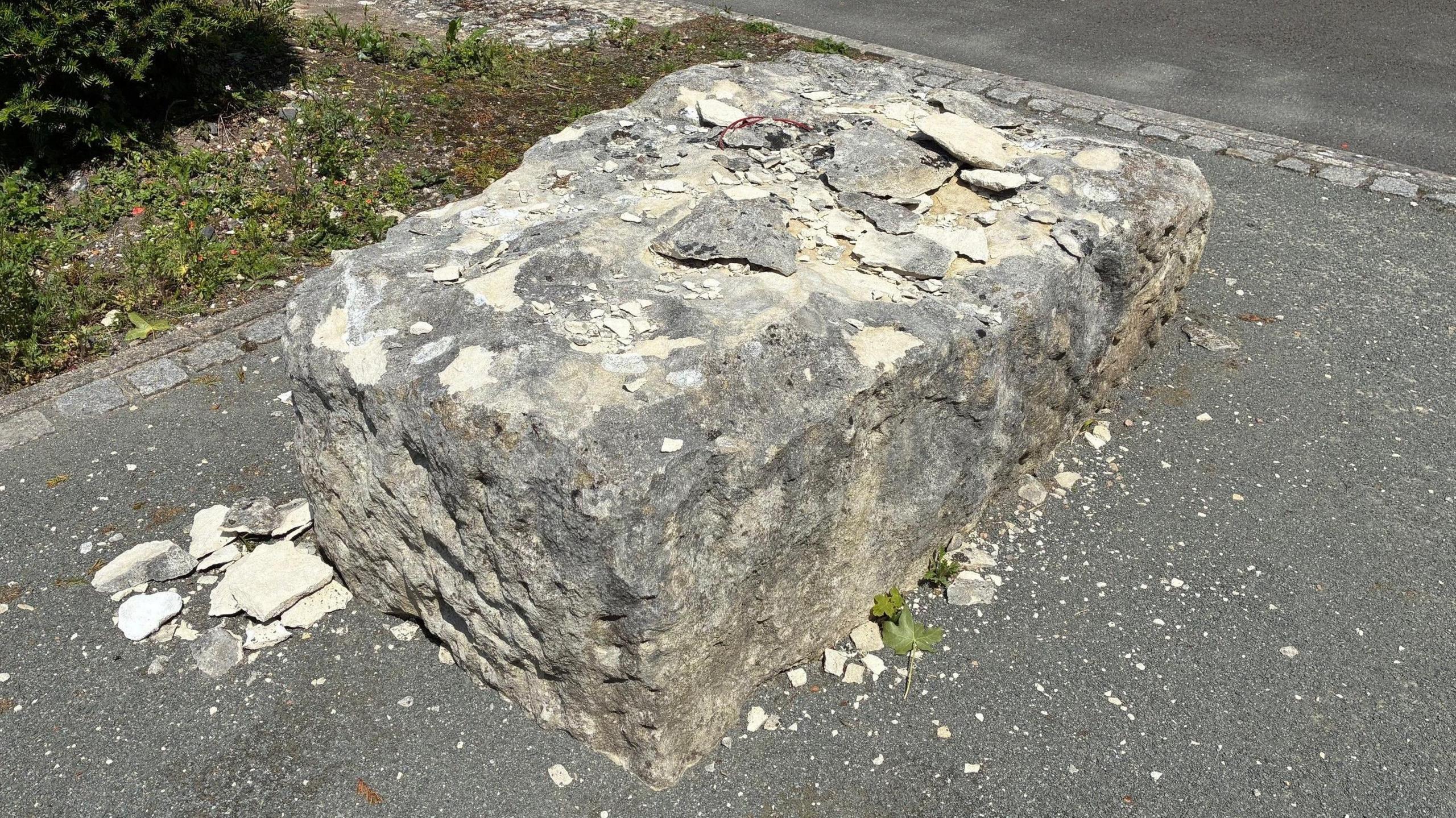A large rectangular boulder on a path. Fragments of chipped rock are on top and next to it.