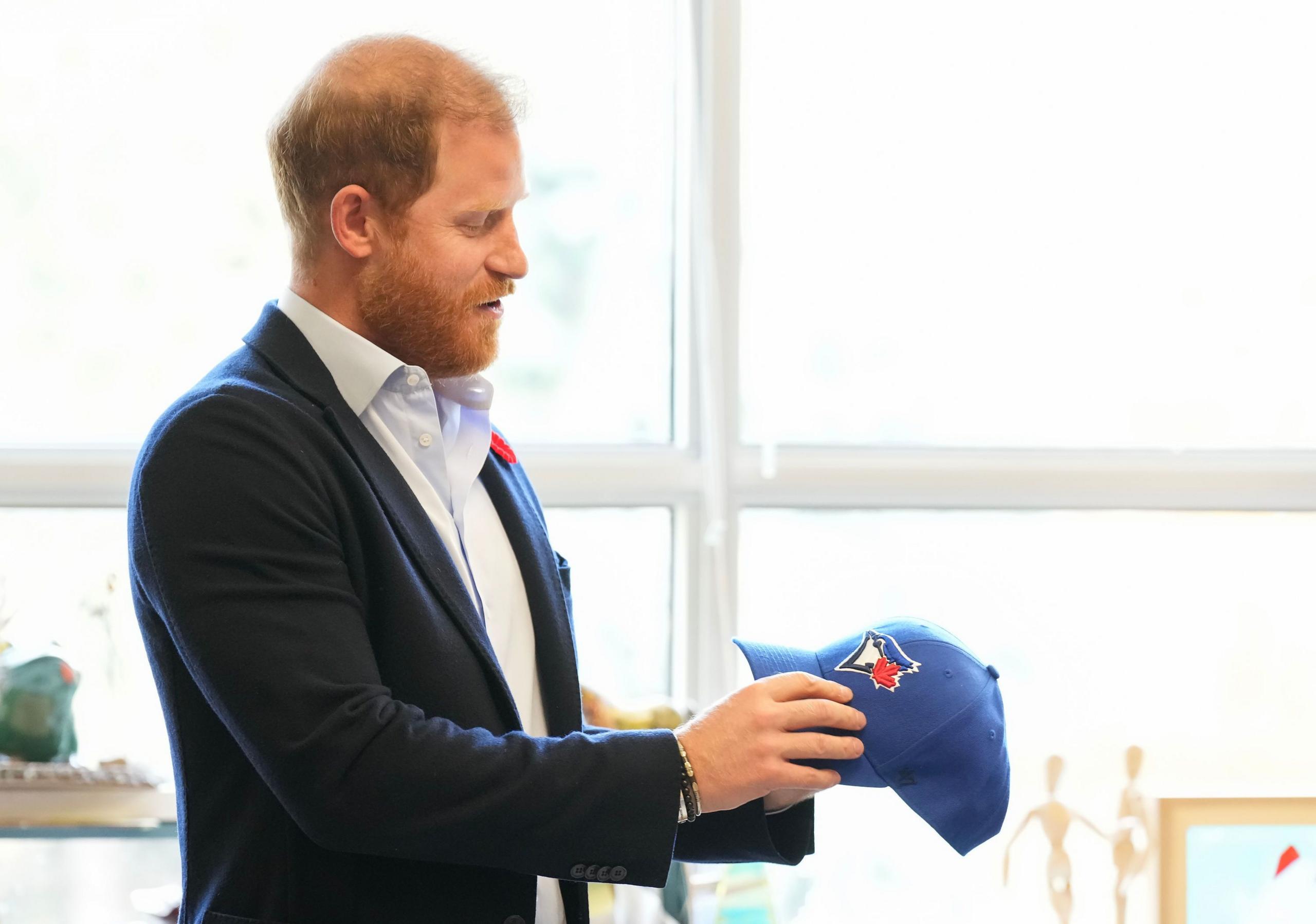 Prince Harry looks at a Toronto Blue Jays hat.