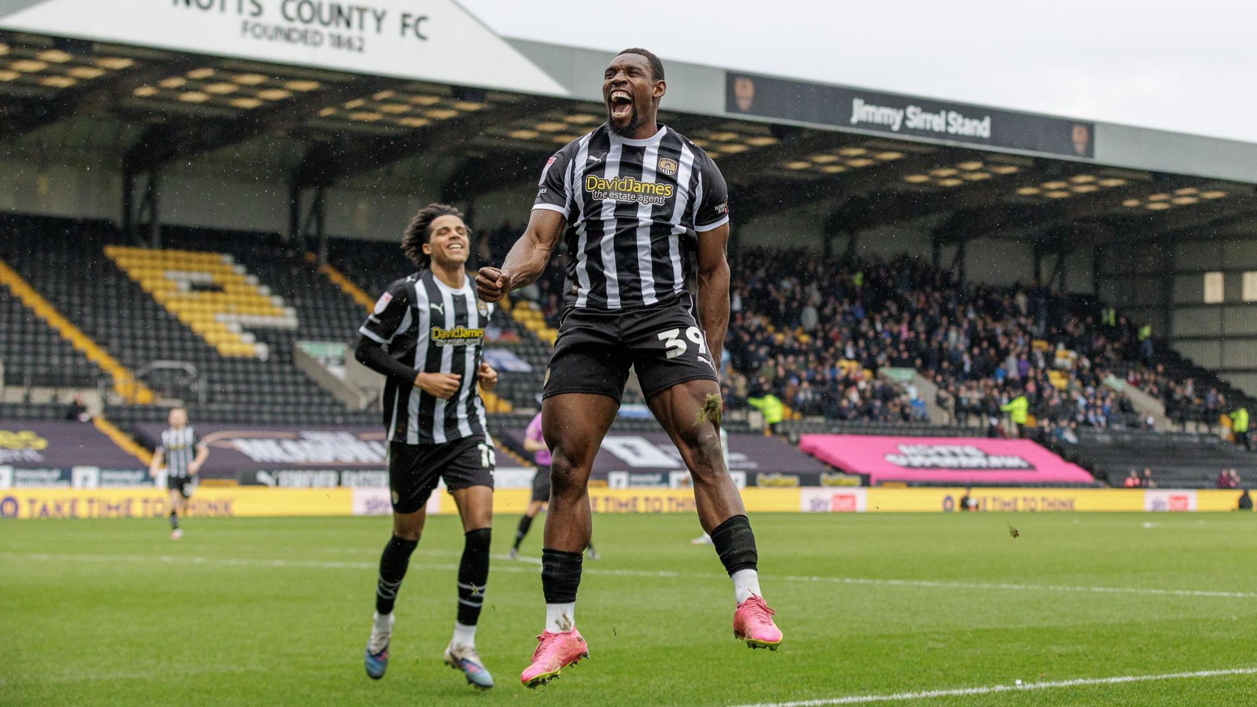 Lee Ndlovu jumps in the air and clenches his fist in his right hand in celebration of a goal