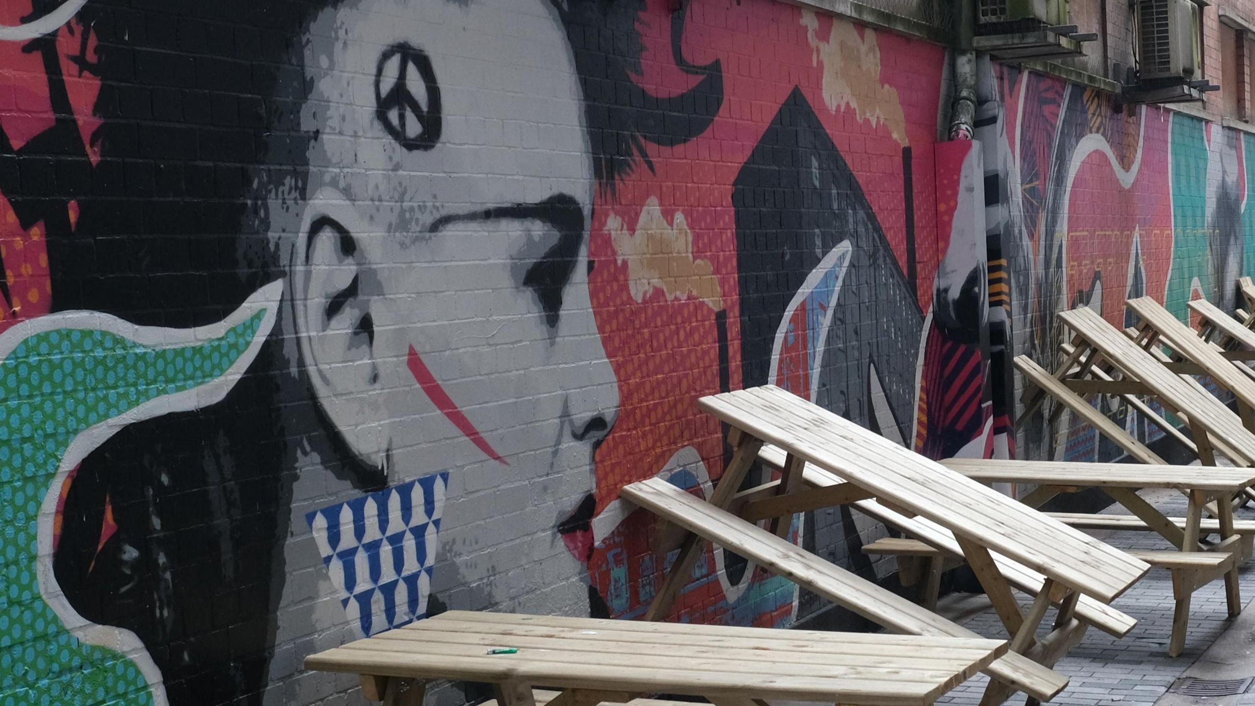 A wall with artwork dedicated to the punk movement with wooden benches leaning against the wall