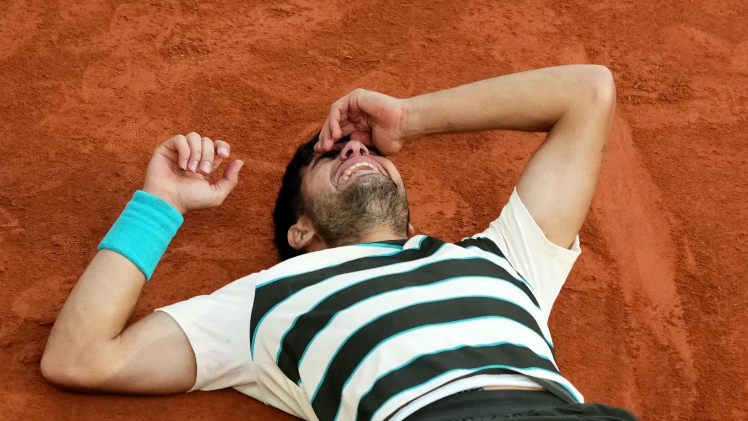 Carlos Alcaraz lies on the court after defending his French Open title