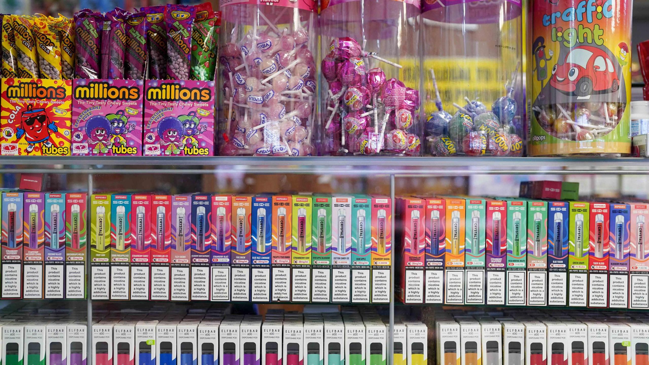 disposable vapes of varying flavours on sale in a store next to sweets.