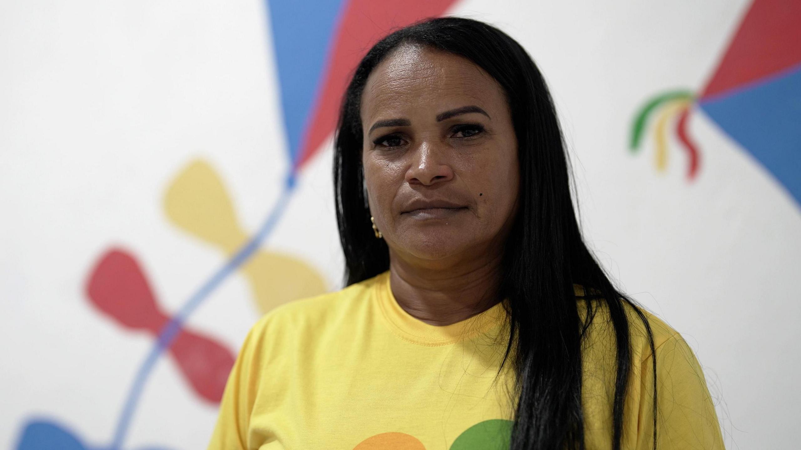 Alessandra Hora looks at the camera. She is wearing a yellow t-shirt and has long black hair.