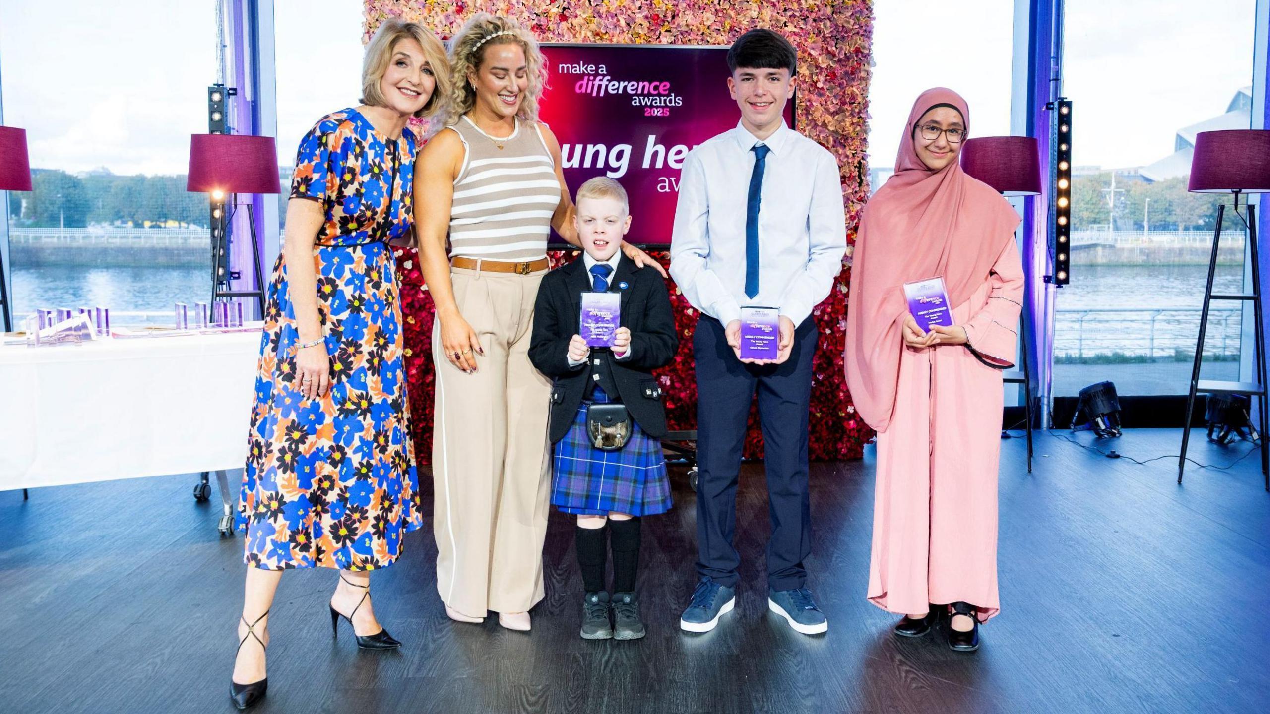 Kaye Adams and Sheli McCoy stand with the highly commended award winners. who are holding their trophies. Behind them is a large TV screen with the words: "Make a Difference Awards".