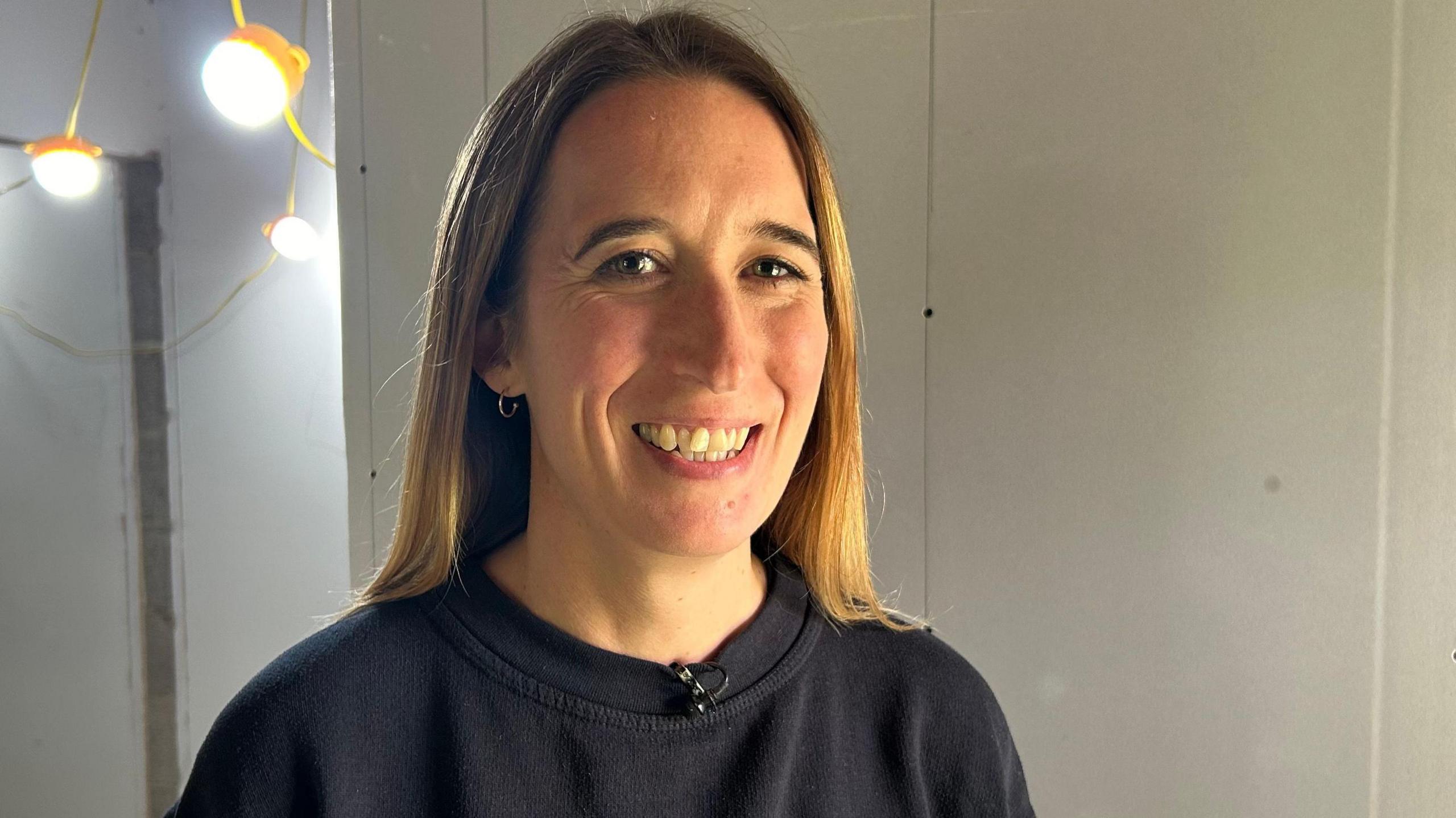 Rachel Jones smiling at the camera, with shoulder-length blonde and brown hair, wearing a black jumper.