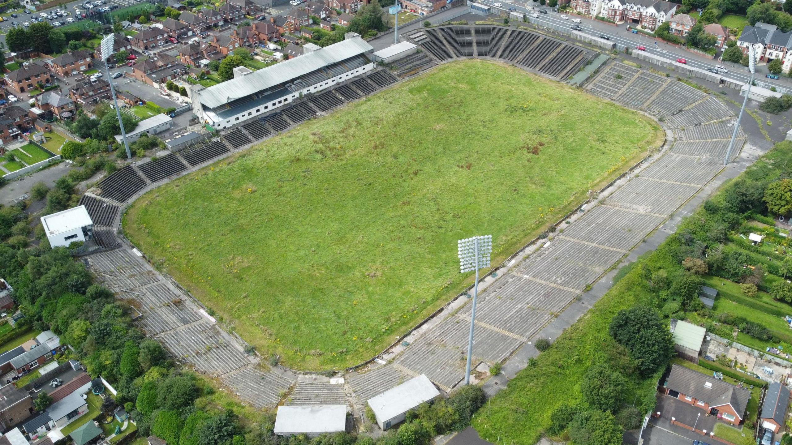 A drone image of Casement Park, a green oval playing field and empty, derelict stands surround it. There are houses all round the park.