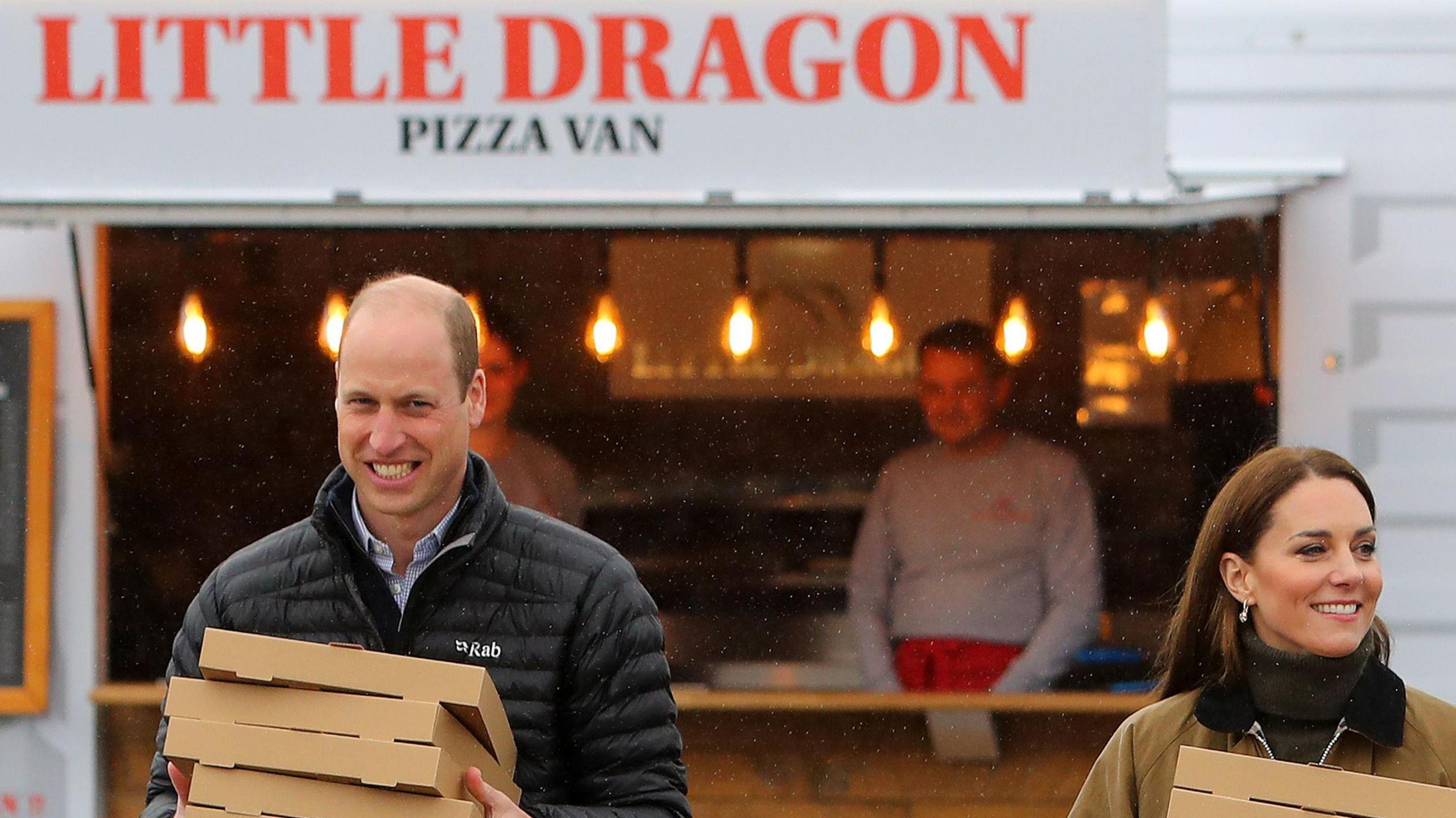 Prince and Princess of Wales holding pizza boxes with the Little Dragons Pizza van behind them, Peter Morris is seen in the van